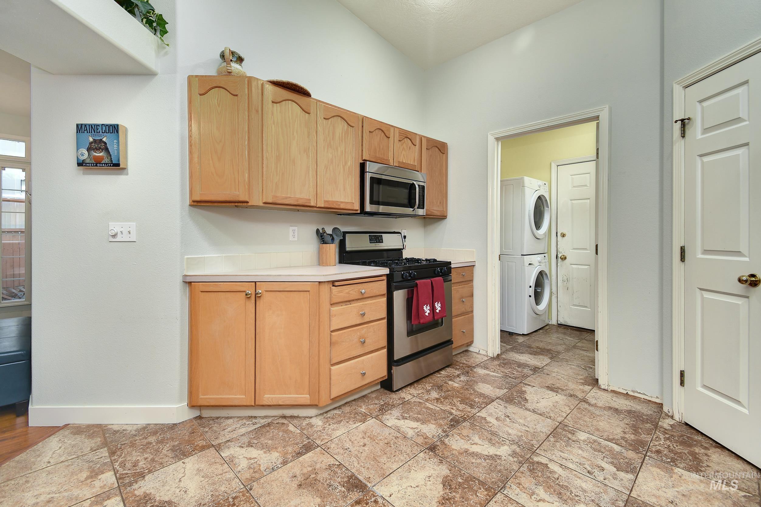 Kitchen with appliances with stainless steel finishes, light countertops, light brown cabinetry, and stacked washer / dryer