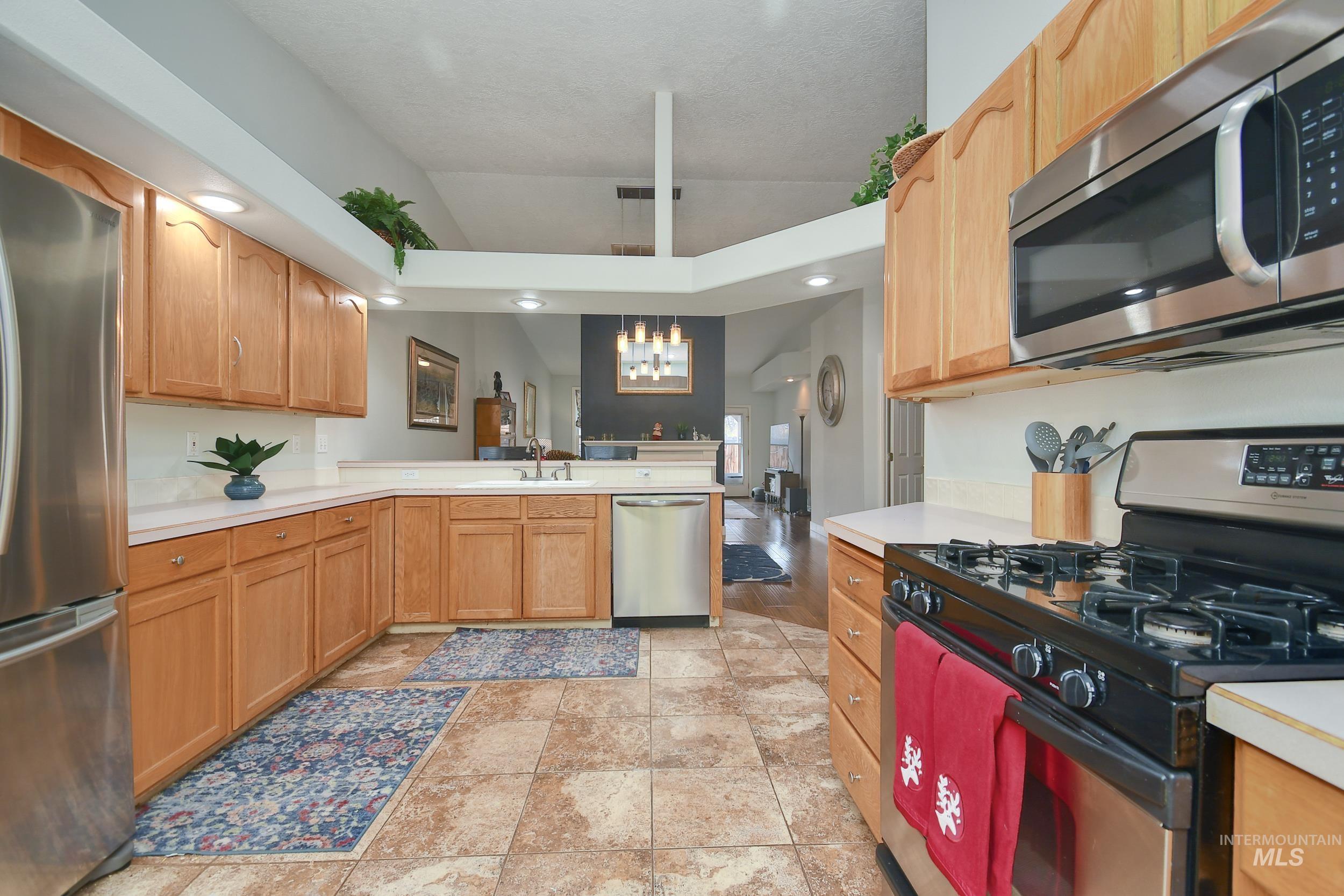 Kitchen featuring stainless steel appliances, light countertops, a chandelier, pendant lighting, and vaulted ceiling