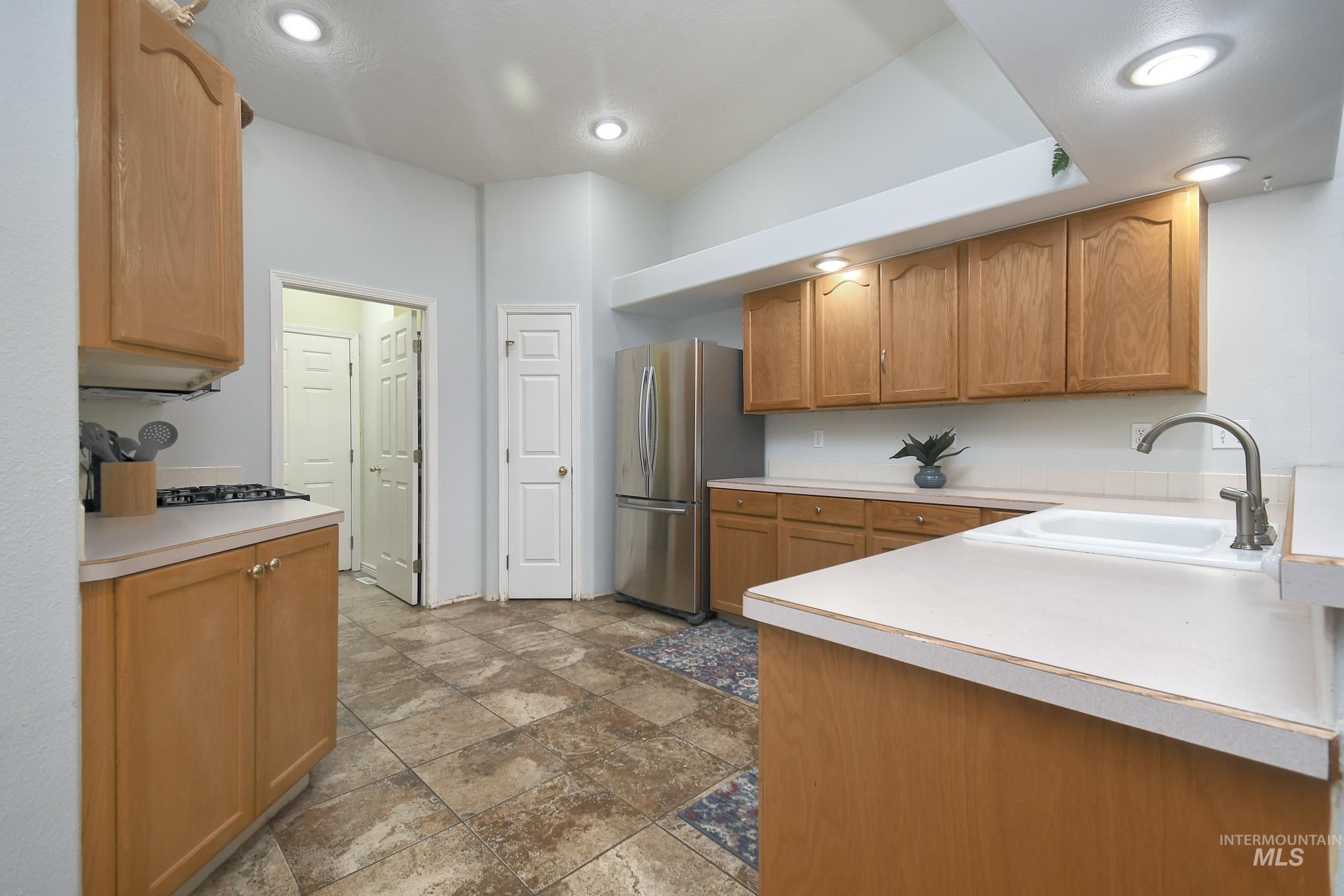 Kitchen with light countertops, freestanding refrigerator, brown cabinets, dark stone finish flooring, and recessed lighting