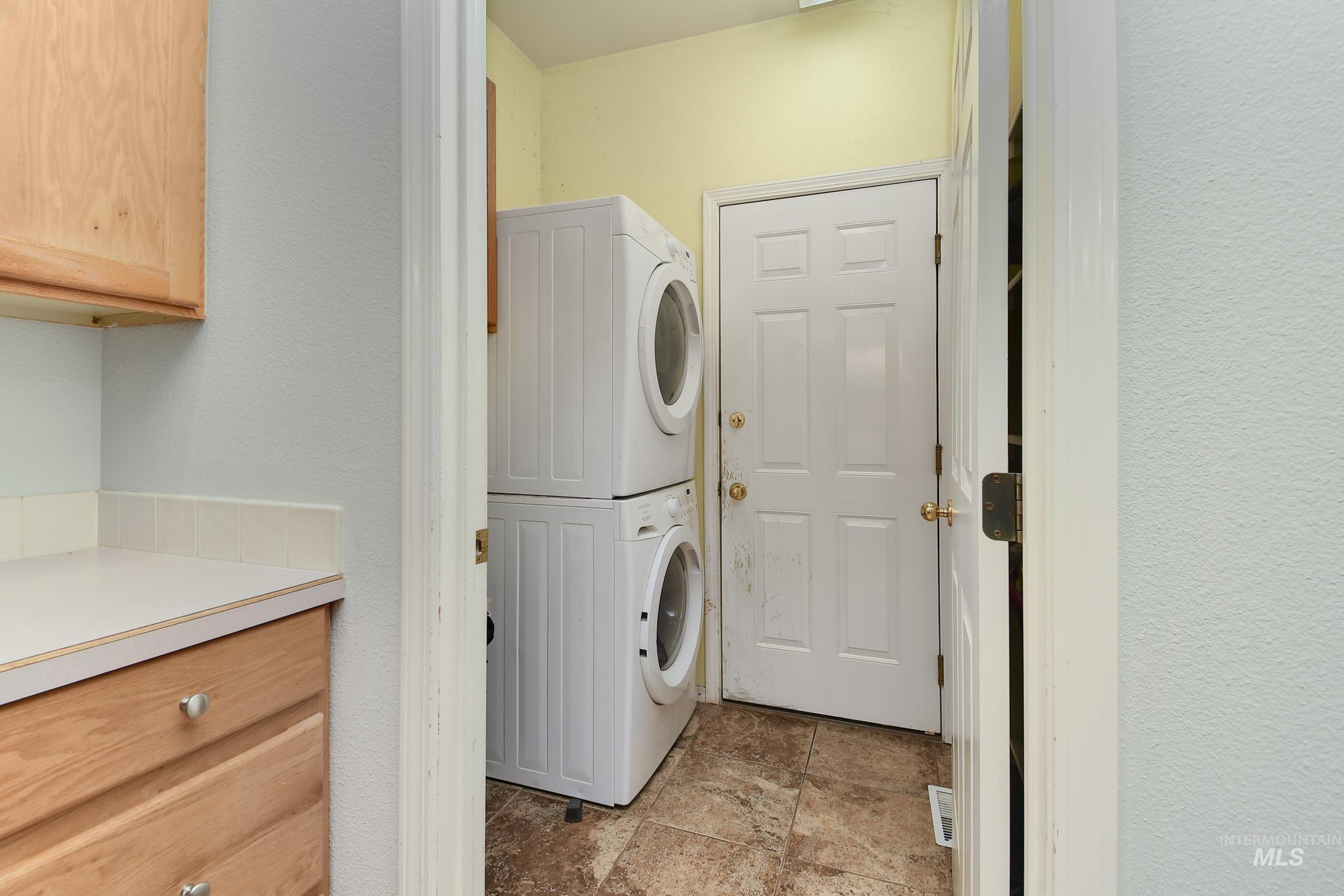 Laundry room featuring stacked washing machine and dryer and light stone finish flooring