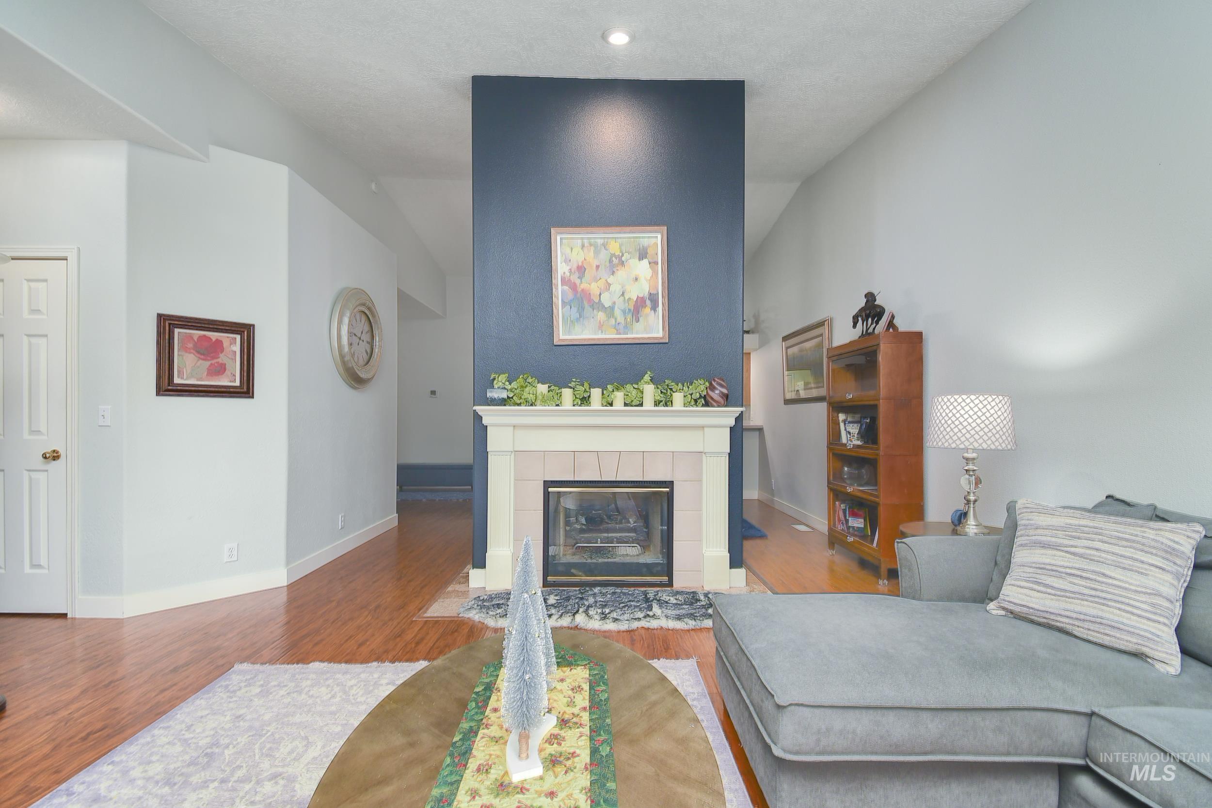 Living room featuring wood finished floors, a tiled fireplace, a textured ceiling, and vaulted ceiling
