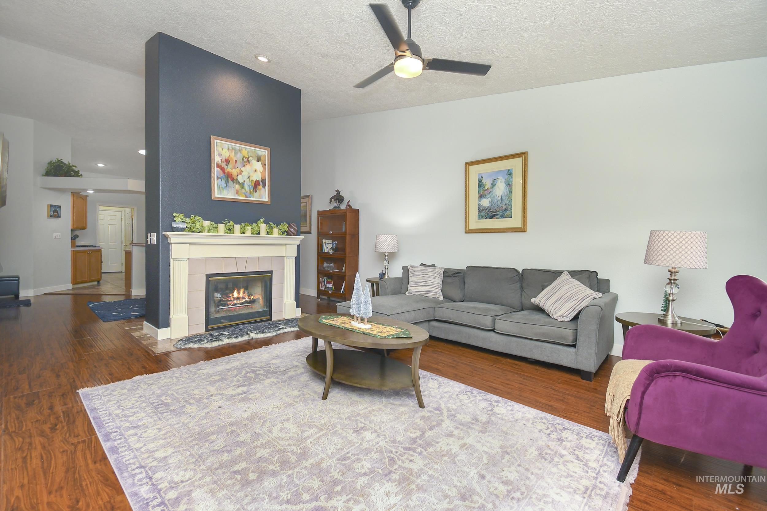 Living room featuring dark wood finished floors, a textured ceiling, recessed lighting, a ceiling fan, and a tile fireplace