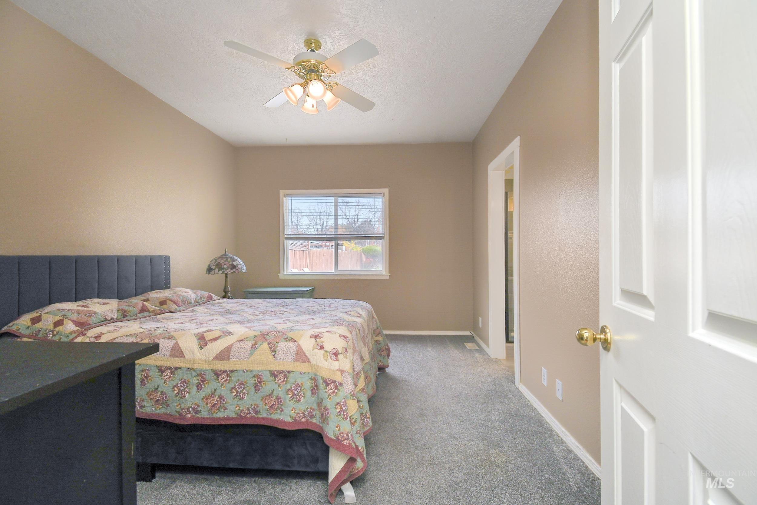Carpeted bedroom featuring ceiling fan and a textured ceiling