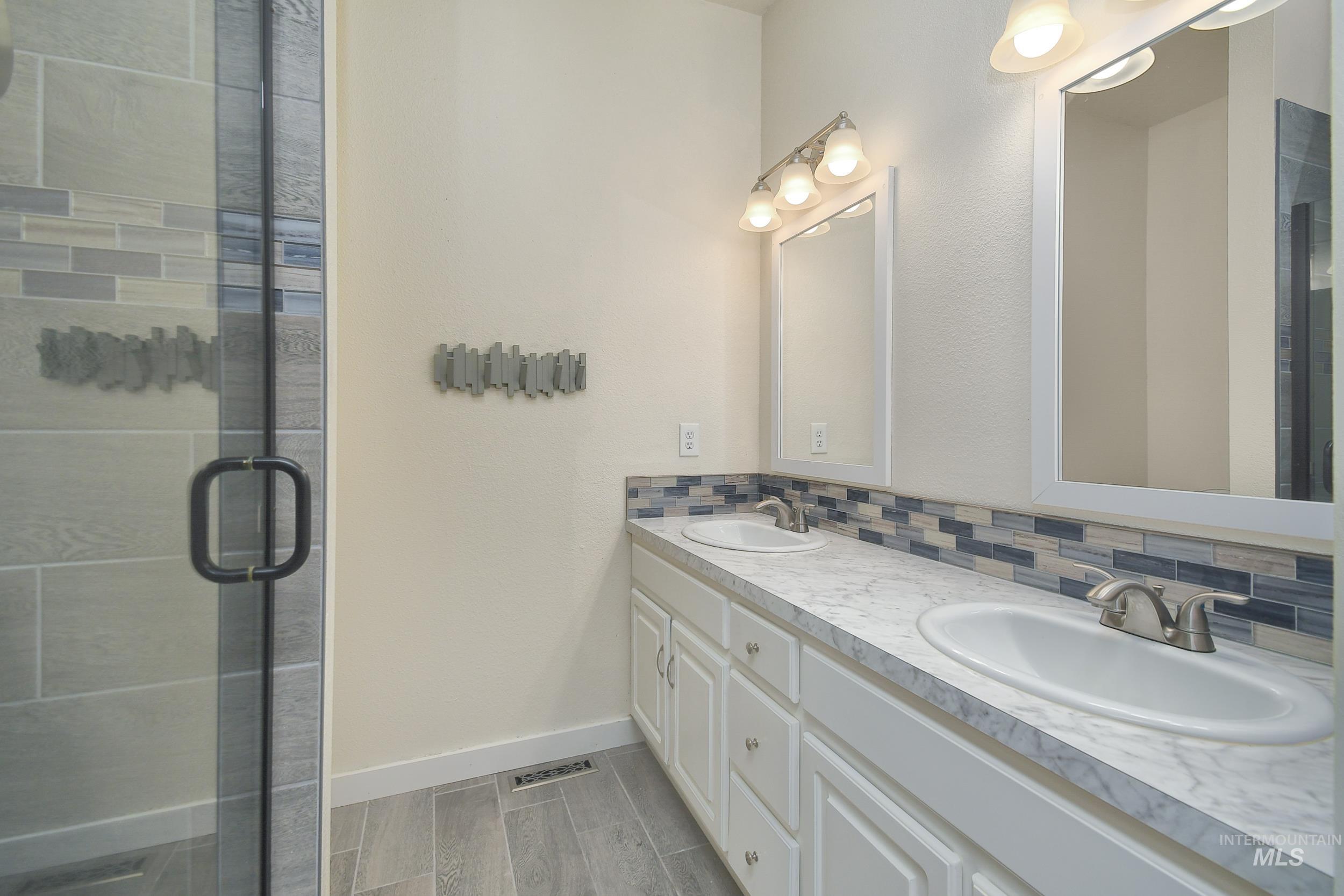 Full bath with backsplash, double vanity, wood finish floors, and a stall shower