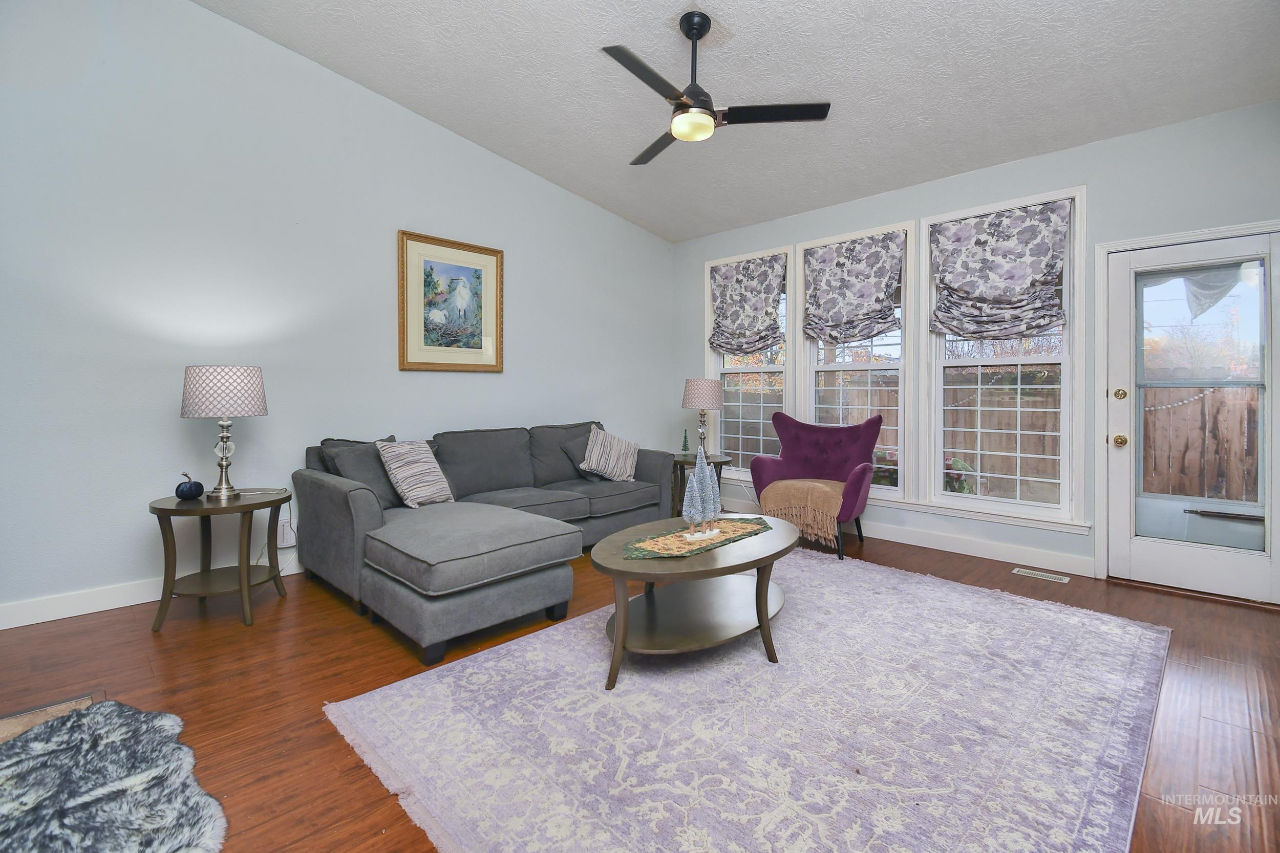 Living area featuring lofted ceiling, a textured ceiling, dark wood-style floors, and a ceiling fan