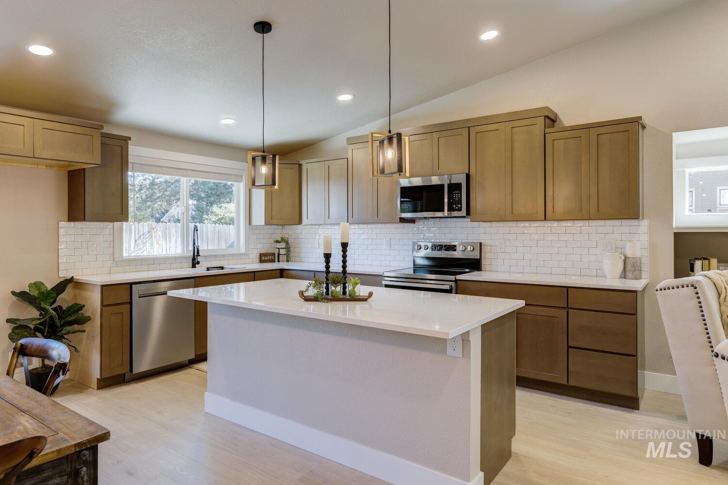 Kitchen featuring a center island, vaulted ceiling, stainless steel appliances, hanging light fixtures, and decorative backsplash