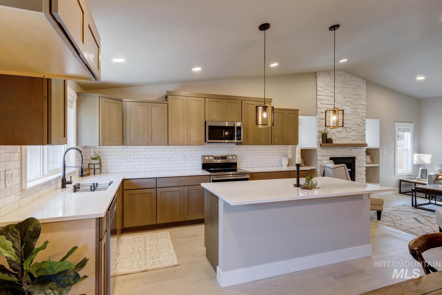 Kitchen with plenty of natural light, vaulted ceiling, tasteful backsplash, appliances with stainless steel finishes, and decorative light fixtures