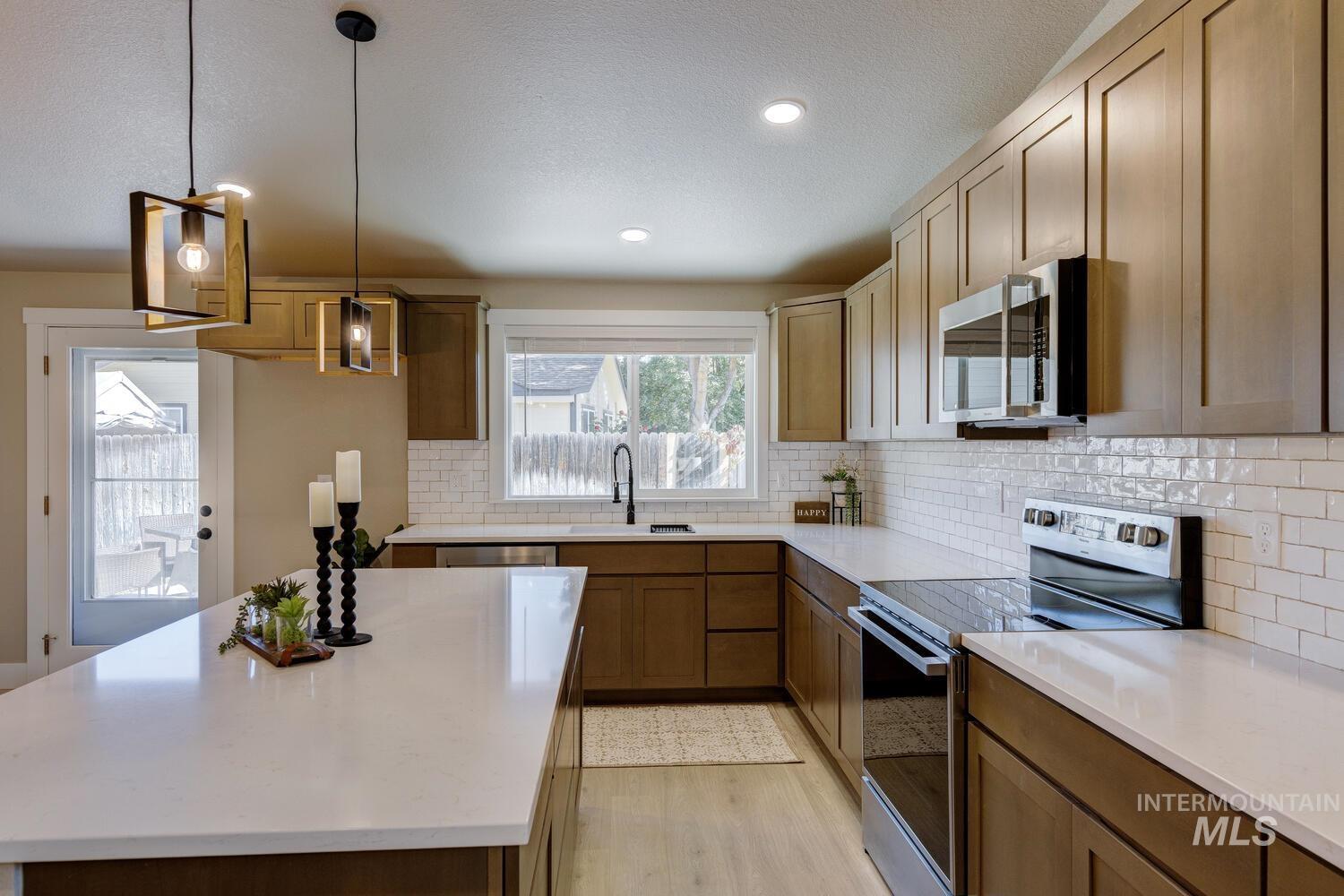 Kitchen featuring stainless steel appliances, a center island, decorative backsplash, light stone countertops, and pendant lighting