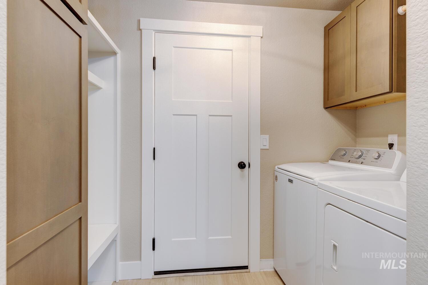 Washroom featuring washer and clothes dryer, light wood-type flooring, and cabinet space