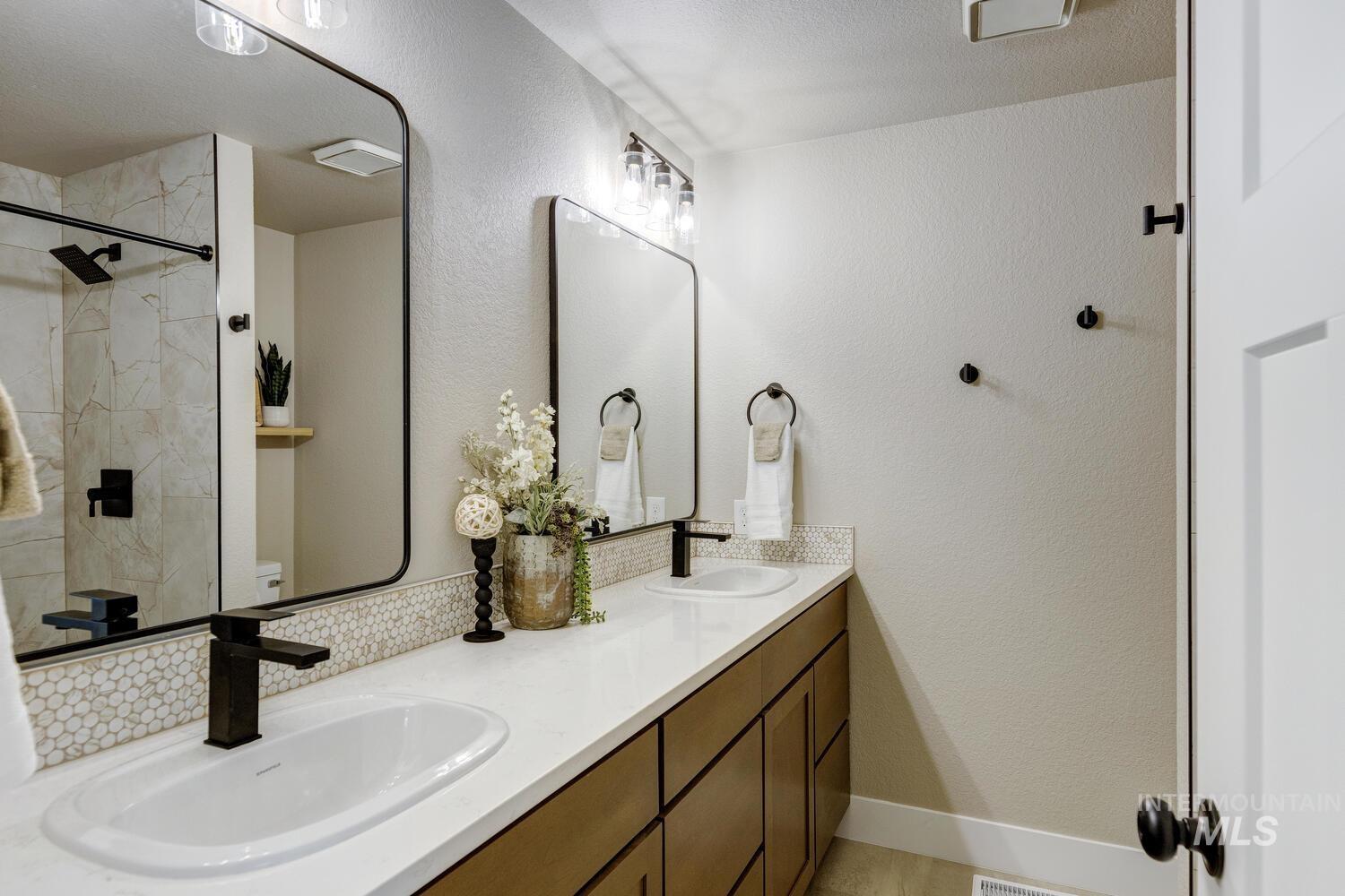 Bathroom featuring a textured wall, double vanity, tiled shower, and a textured ceiling