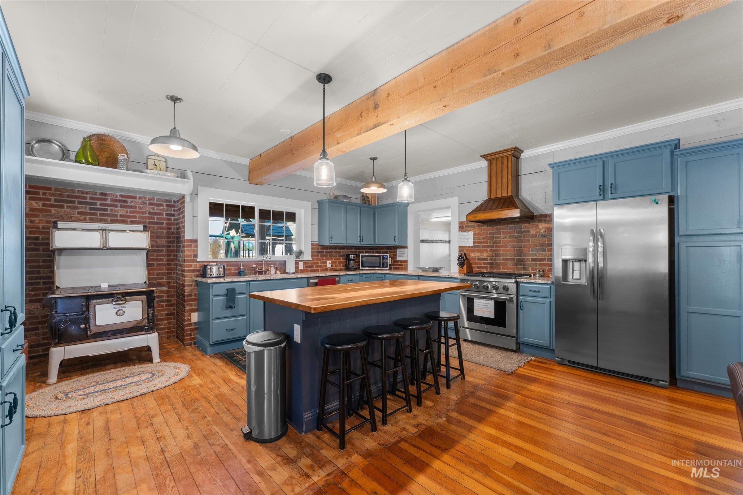 Kitchen with blue cabinets, wood counters, appliances with stainless steel finishes, ornamental molding, and decorative light fixtures