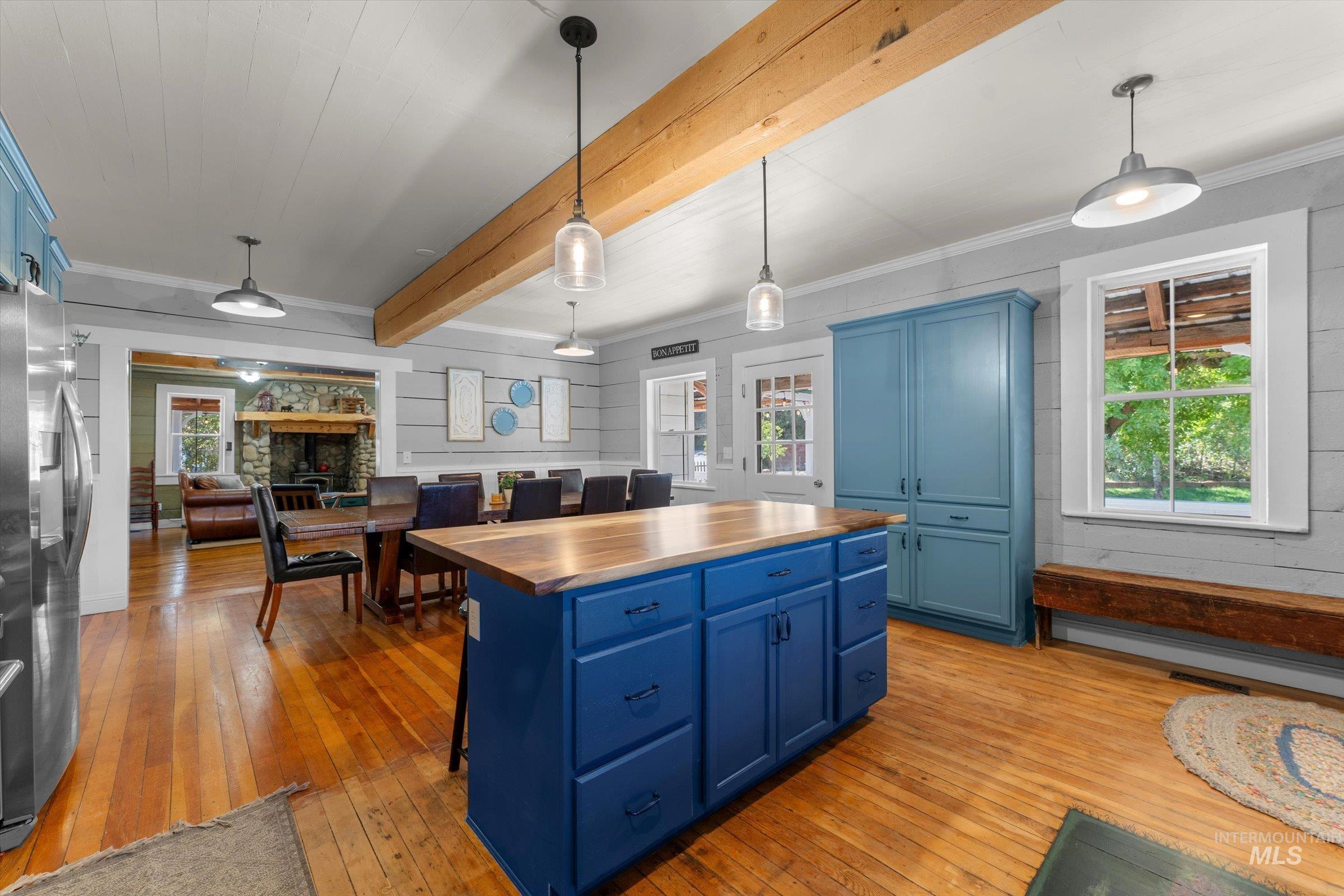 Kitchen with blue cabinetry, butcher block countertops, decorative light fixtures, light wood finished floors, and beamed ceiling