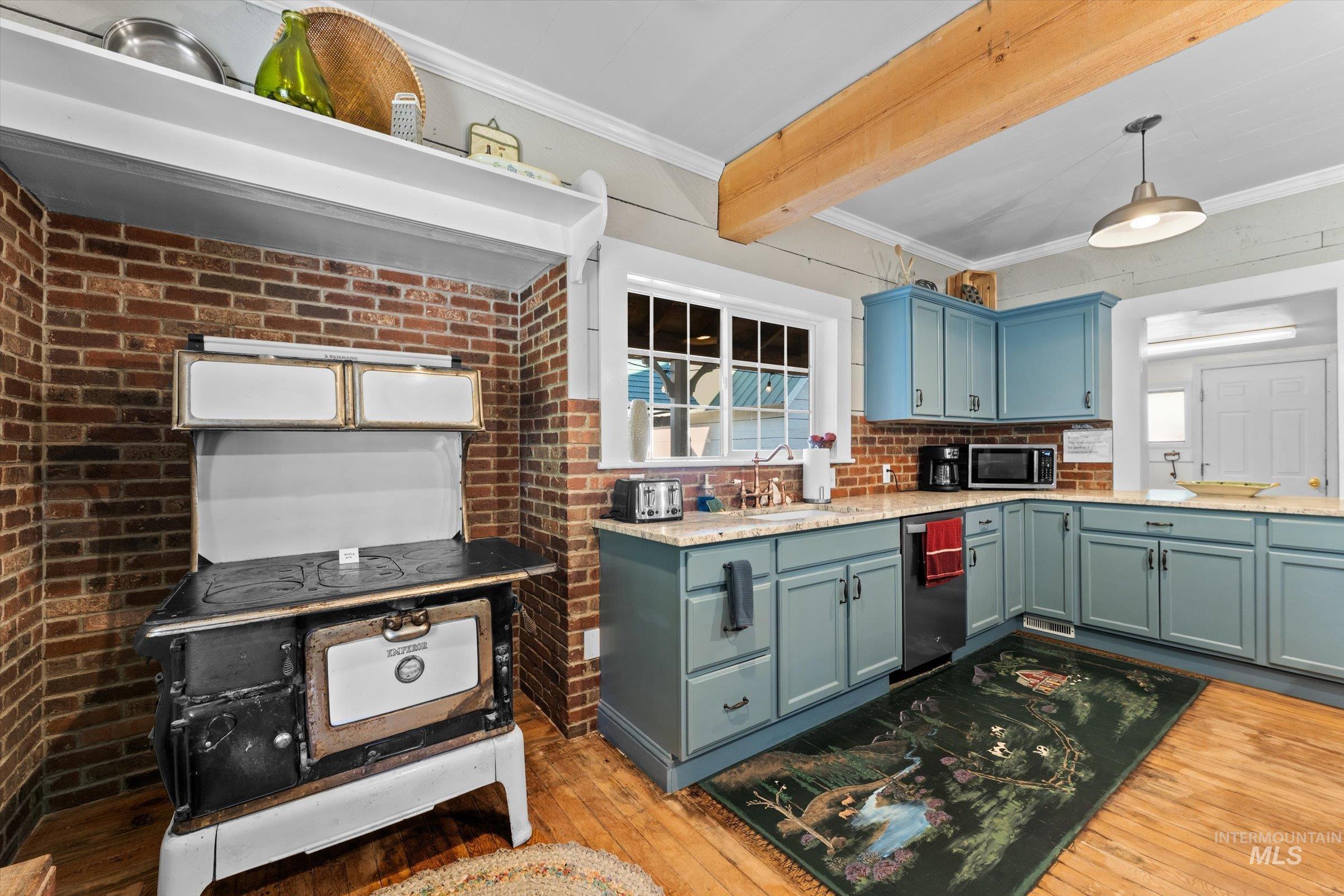 Kitchen with light wood-style flooring, crown molding, pendant lighting, light stone counters, and appliances with stainless steel finishes