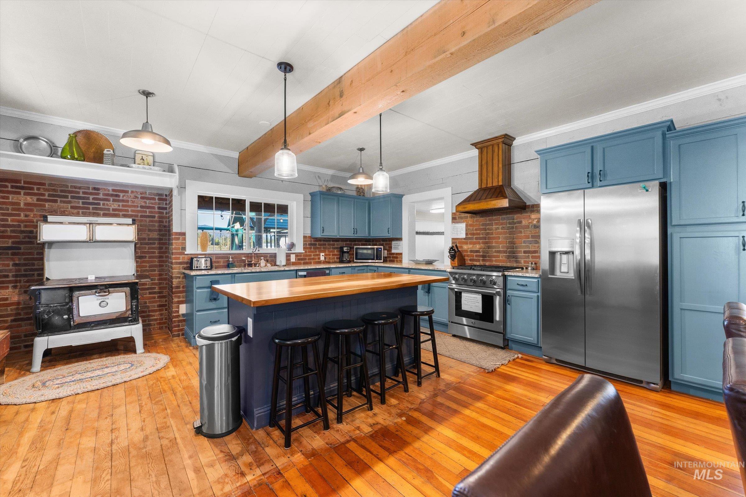 Kitchen featuring blue cabinetry, stainless steel appliances, crown molding, a kitchen bar, and hanging light fixtures