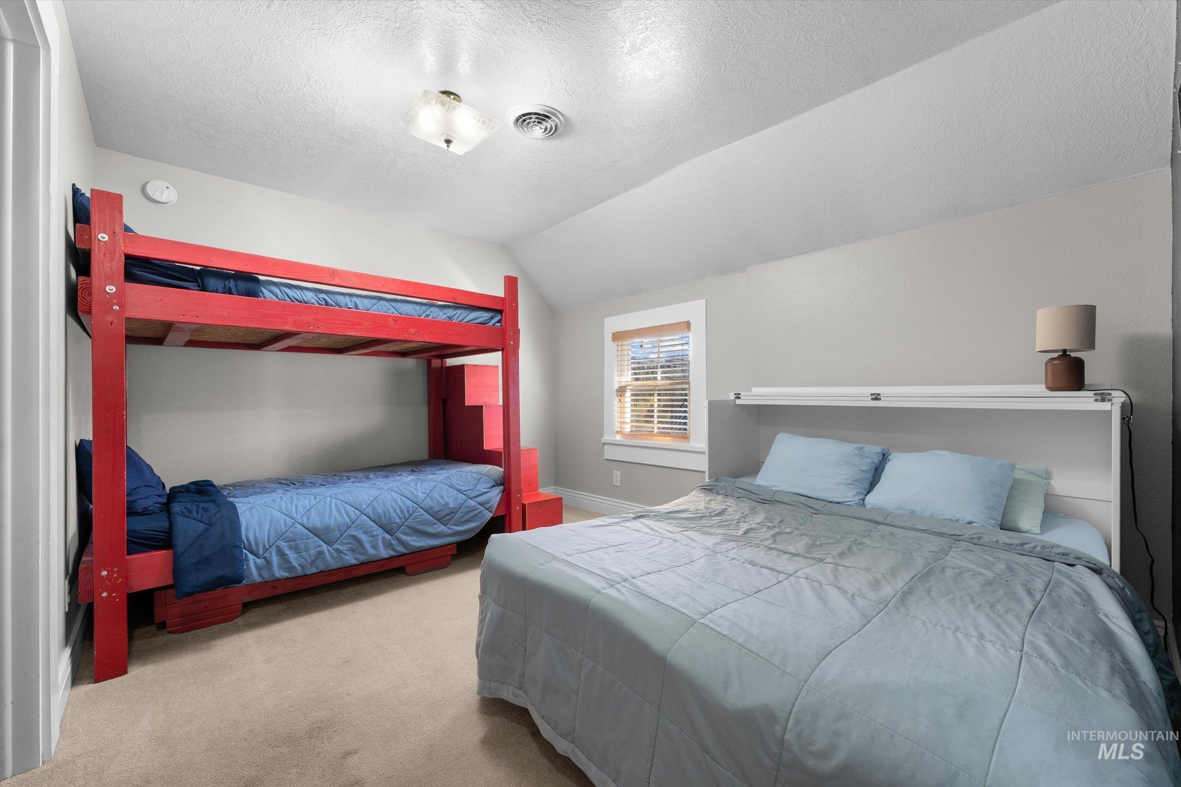 Bedroom with vaulted ceiling, carpet, and a textured ceiling