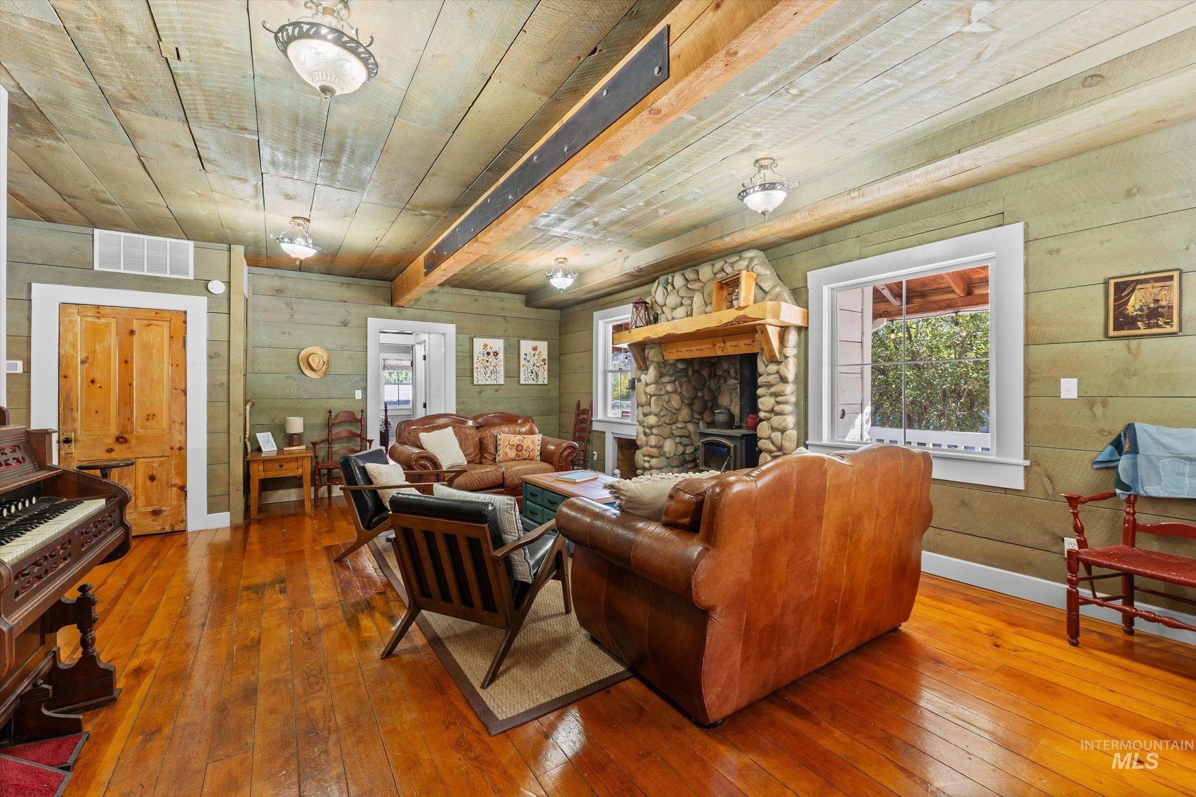 Living area featuring hardwood / wood-style flooring, wood walls, a wooden ceiling with exposed beams, and a wood stove
