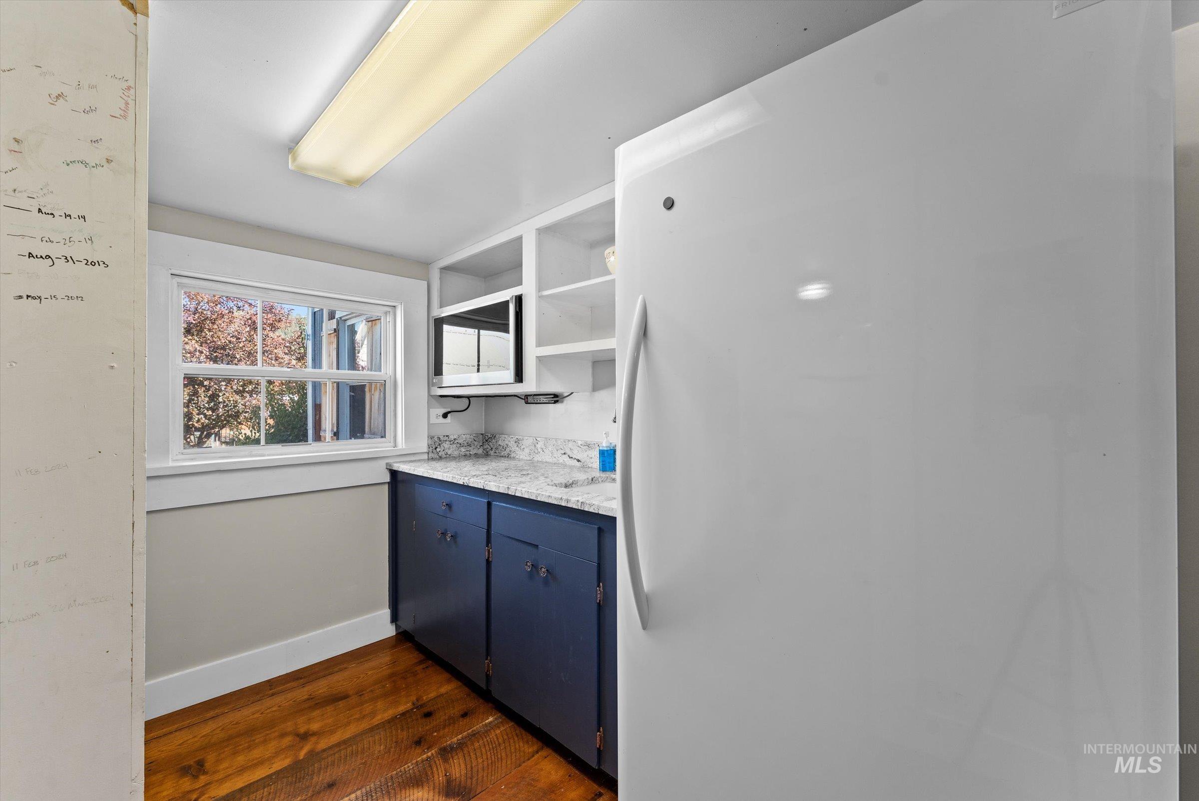 Kitchen with freestanding refrigerator, dark wood finished floors, open shelves, blue cabinetry, and light stone countertops