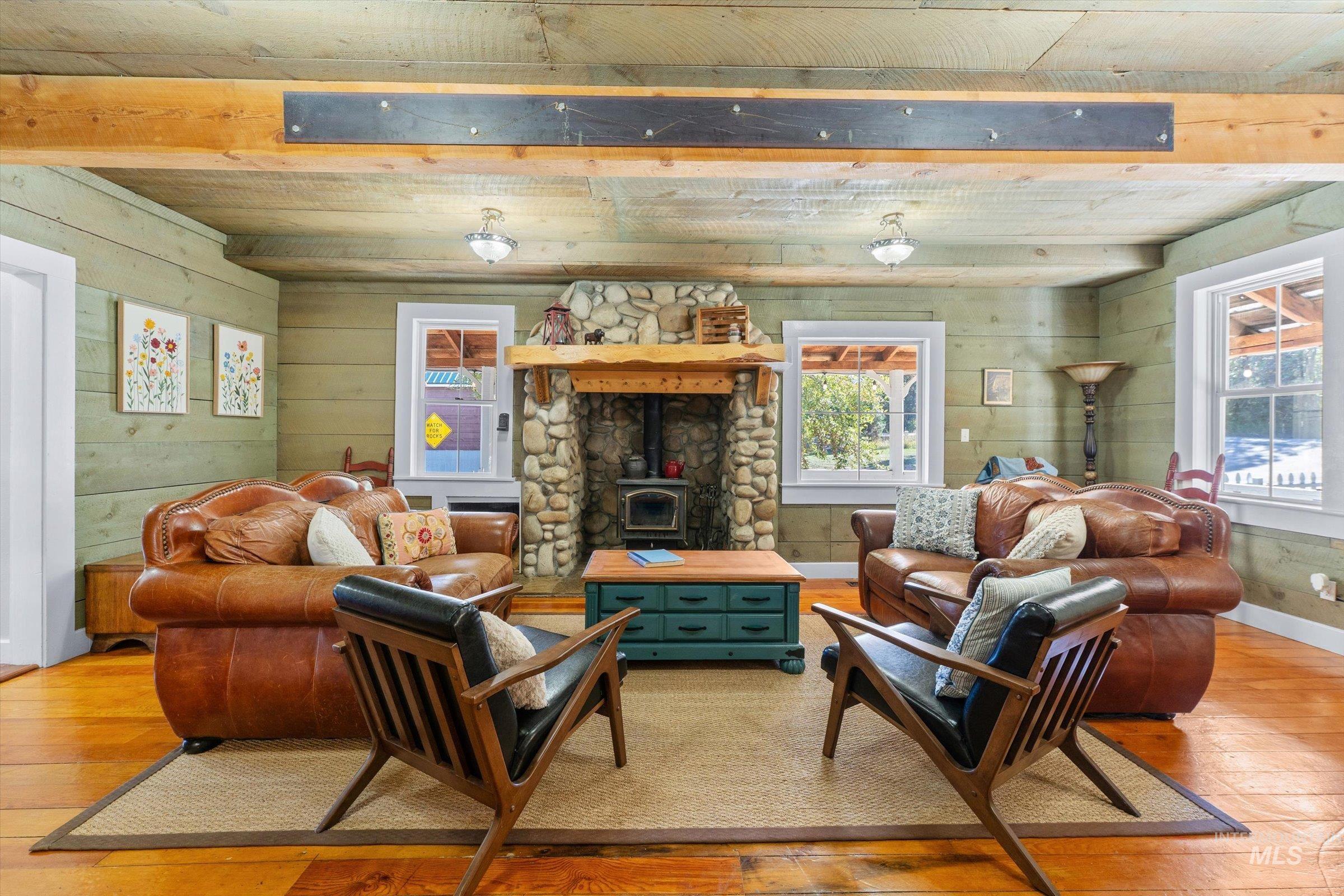 Living area with hardwood / wood-style floors, a wood stove, wood walls, and beam ceiling