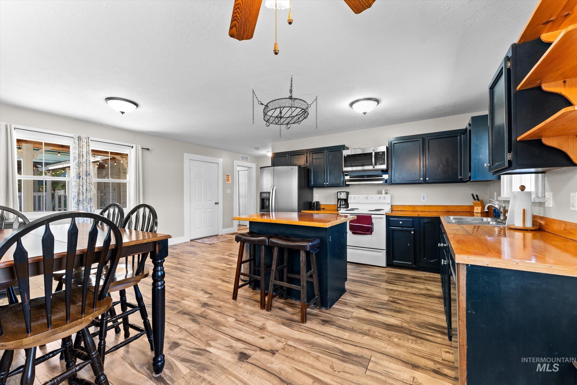 Kitchen featuring open shelves, stainless steel appliances, light wood-style floors, a ceiling fan, and dark cabinets