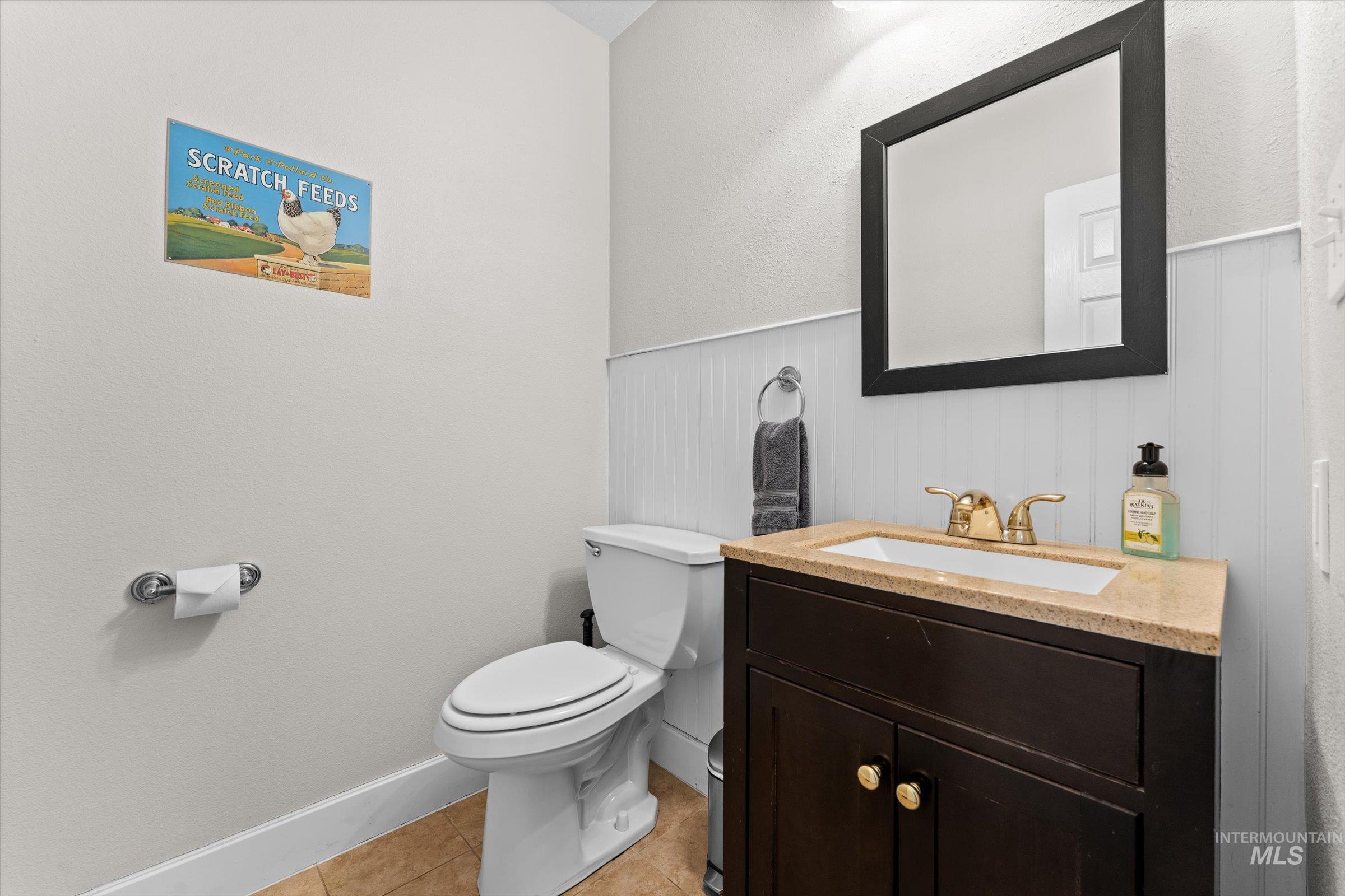 Bathroom with a textured wall, vanity, light tile patterned flooring, and a wainscoted wall