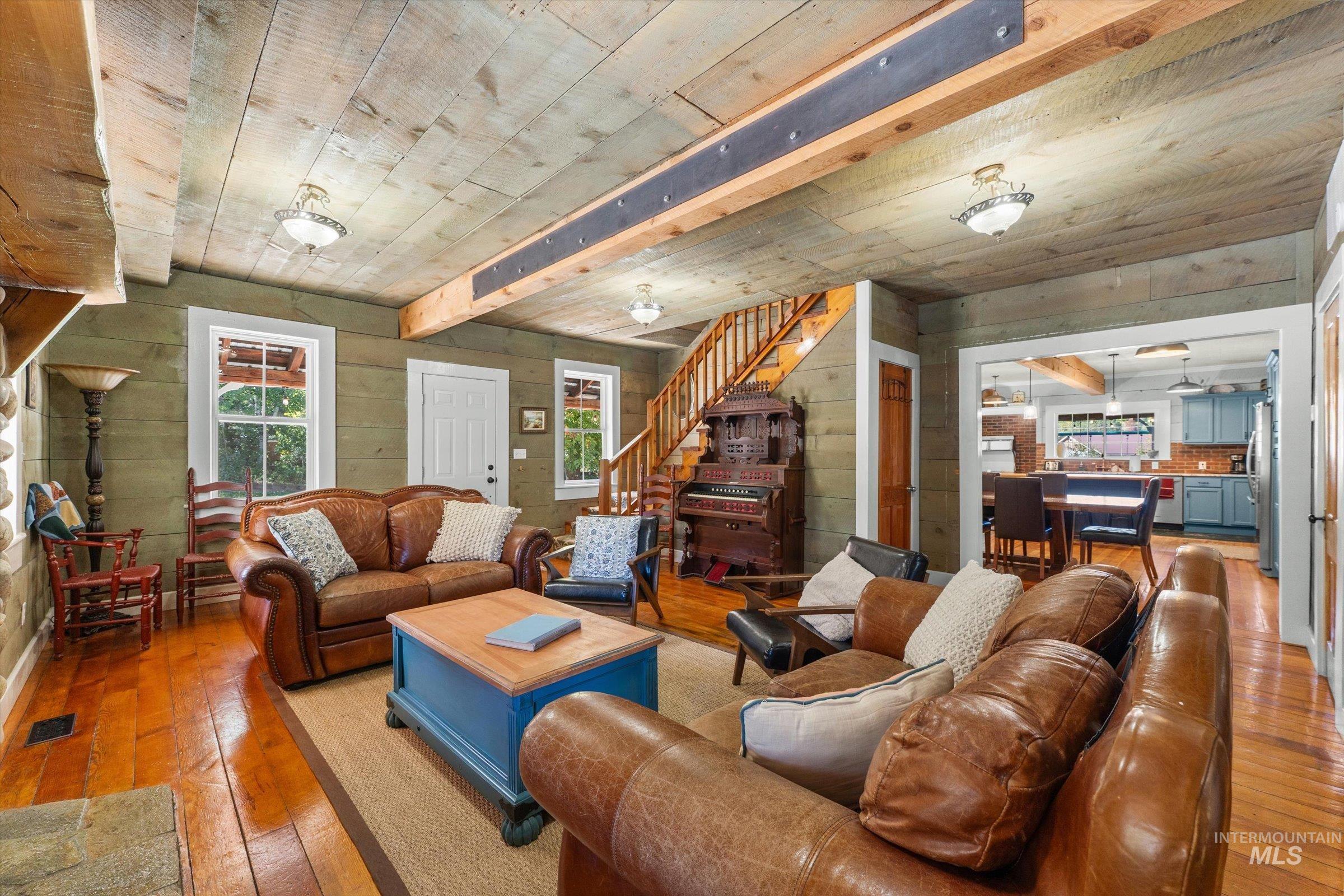 Living room featuring light wood-type flooring, wooden walls, stairs, and a wooden ceiling with exposed beams