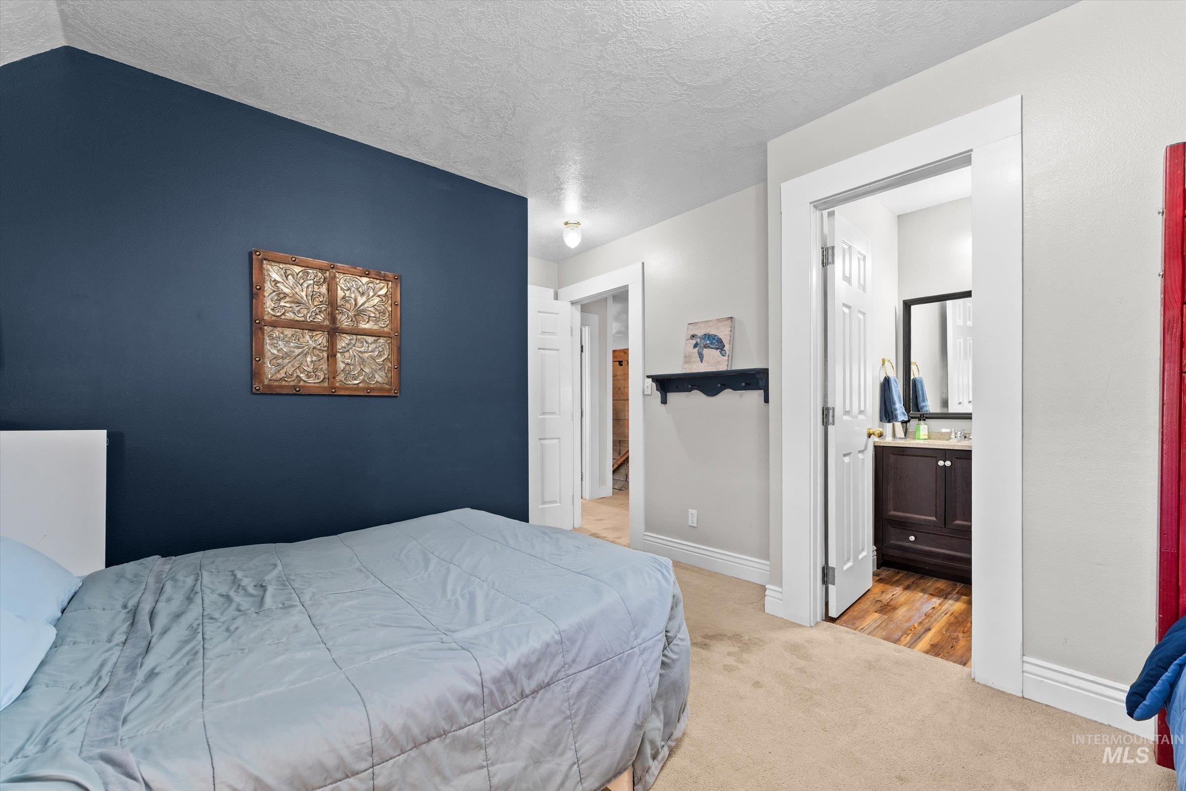 Bedroom with light carpet, a textured ceiling, and ensuite bath