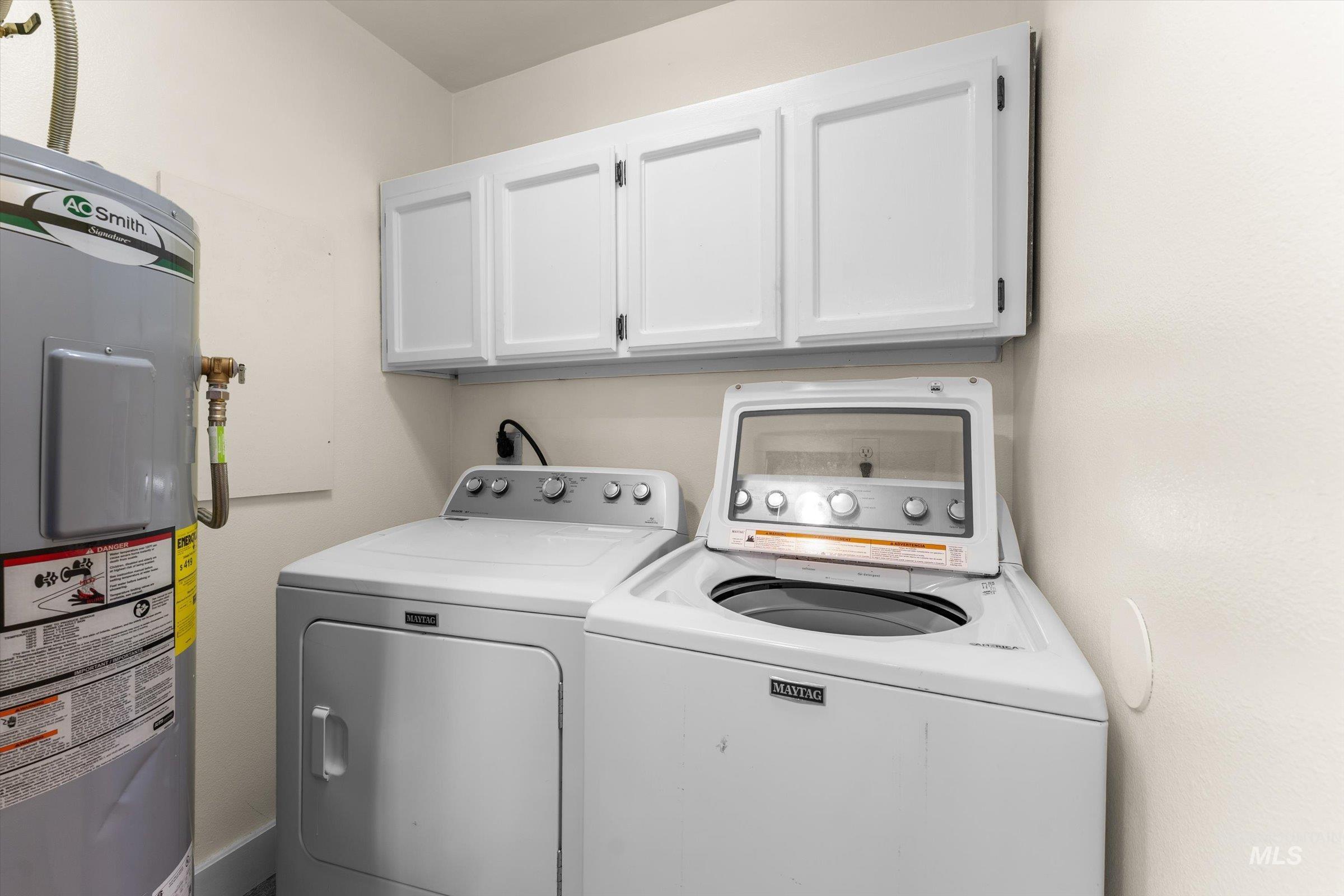 Laundry area featuring electric water heater, cabinet space, and washing machine and clothes dryer