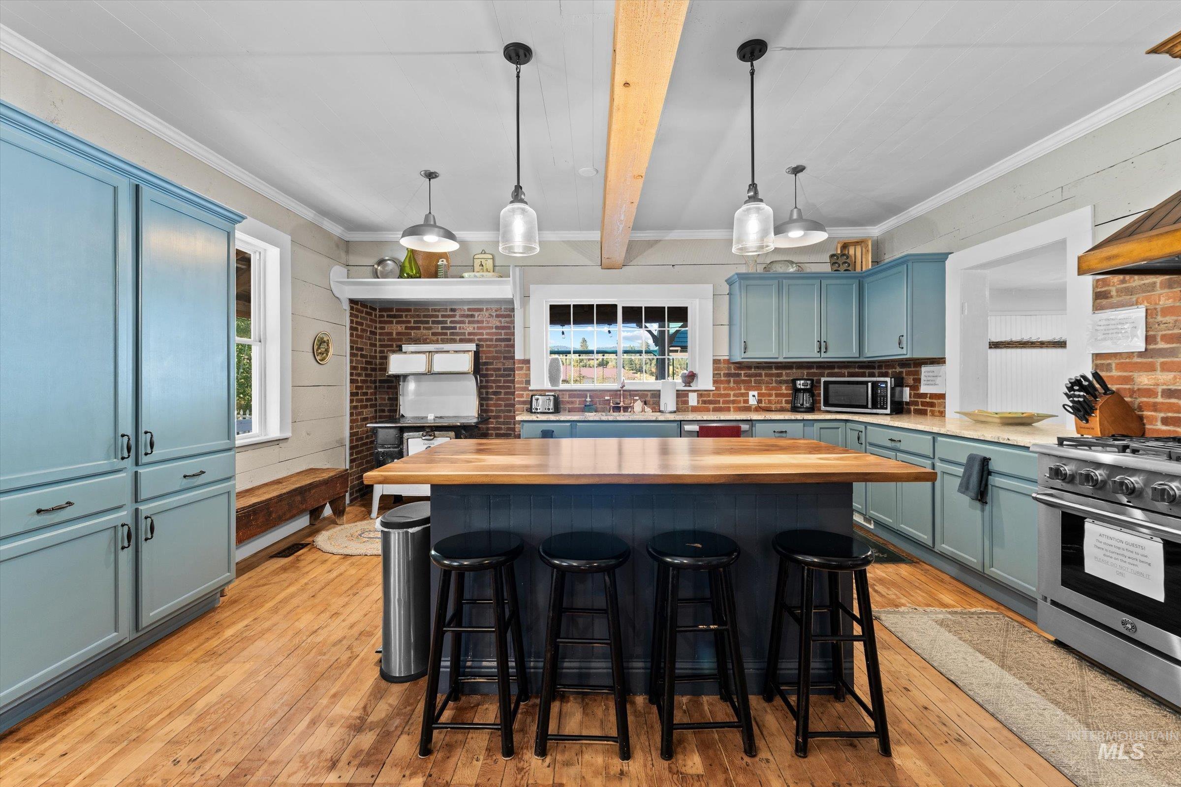 Kitchen with light wood finished floors, a kitchen island, hanging light fixtures, a kitchen bar, and stainless steel appliances