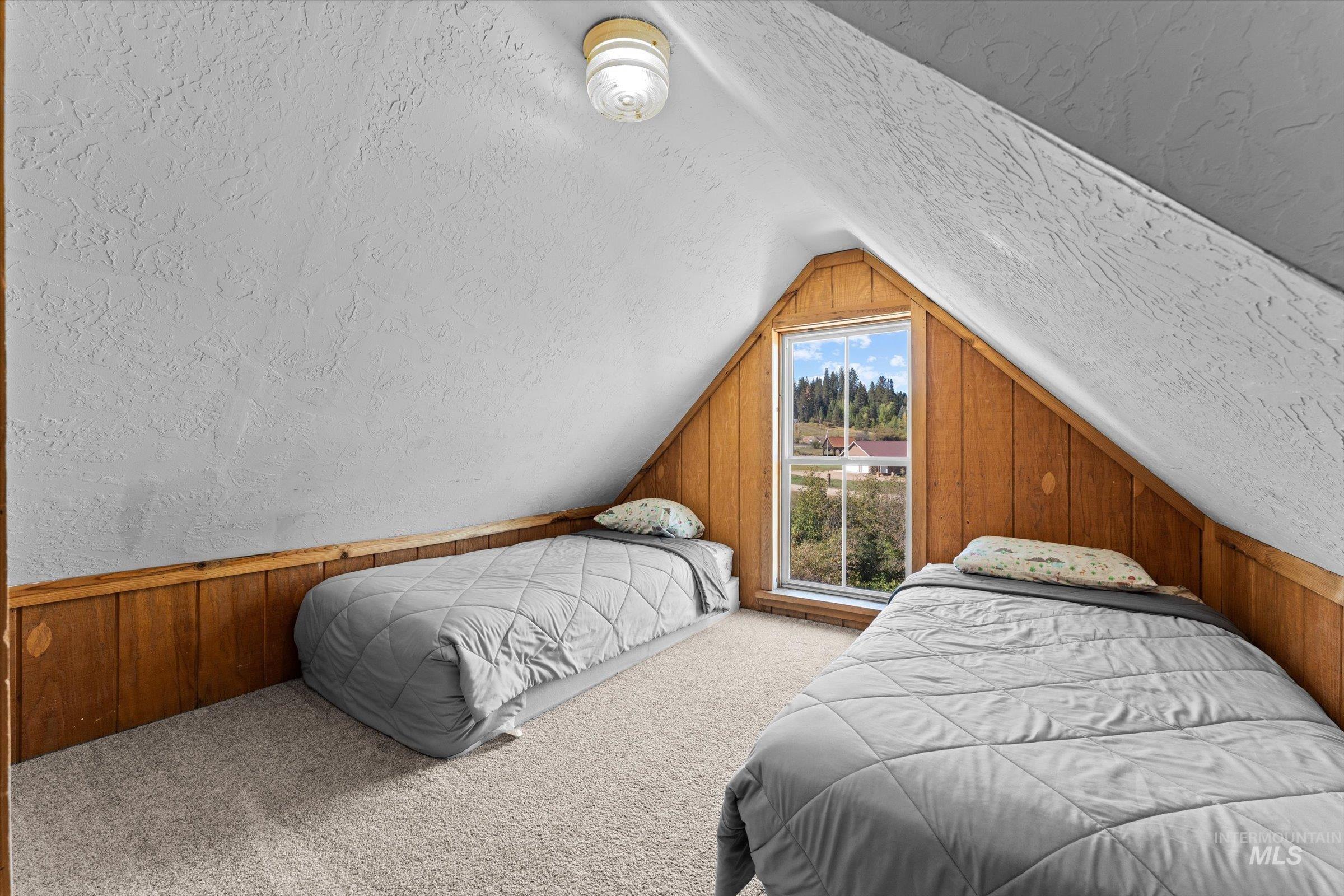 Carpeted bedroom featuring wood walls, a textured ceiling, lofted ceiling, a textured wall, and wainscoting