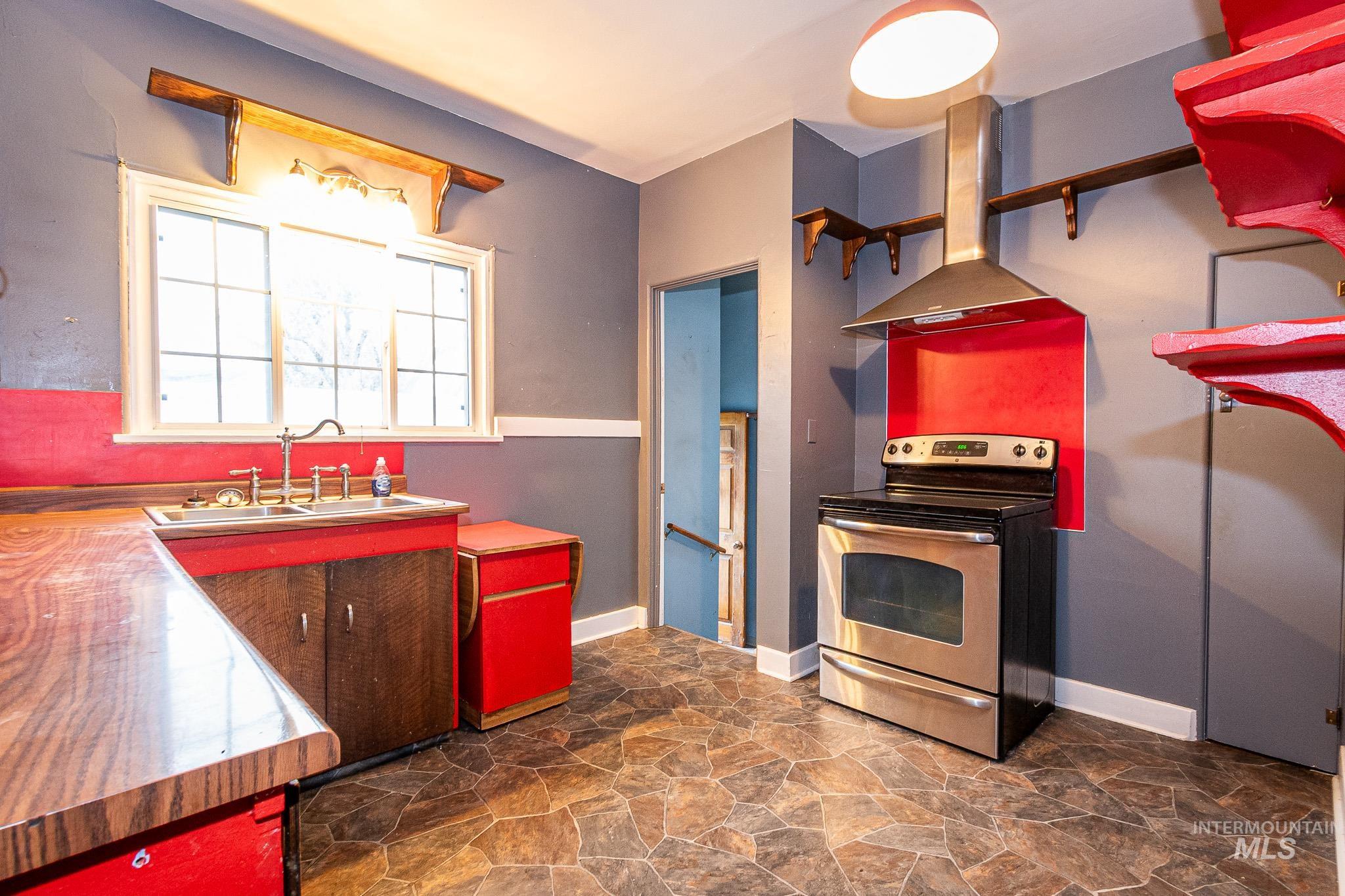 Kitchen featuring stone finish flooring, stainless steel range with electric stovetop, wall chimney range hood, and red cabinets