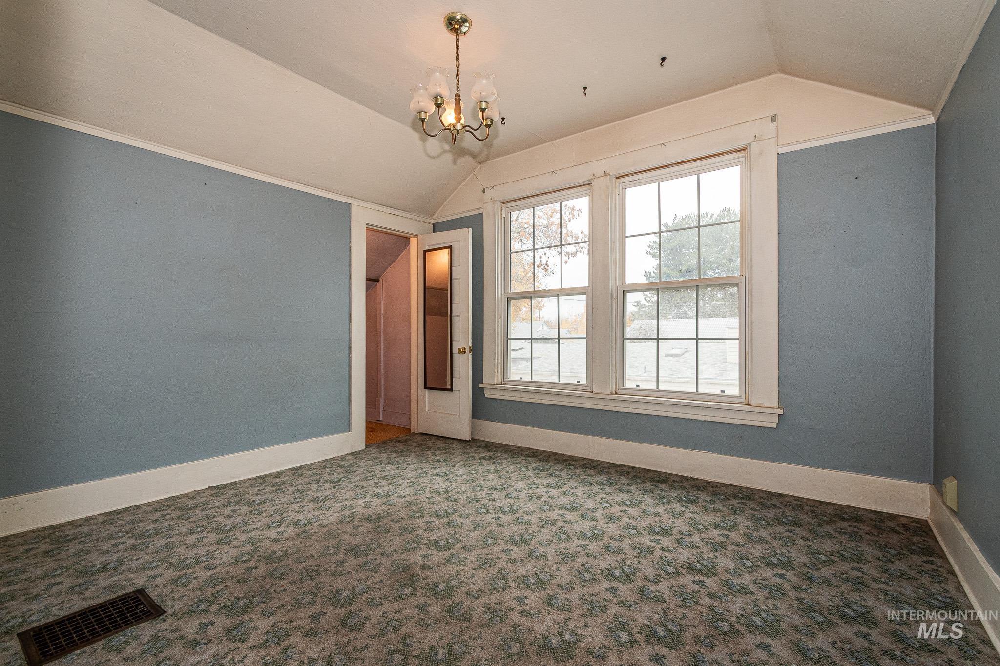 Empty room featuring lofted ceiling, a chandelier, and carpet flooring