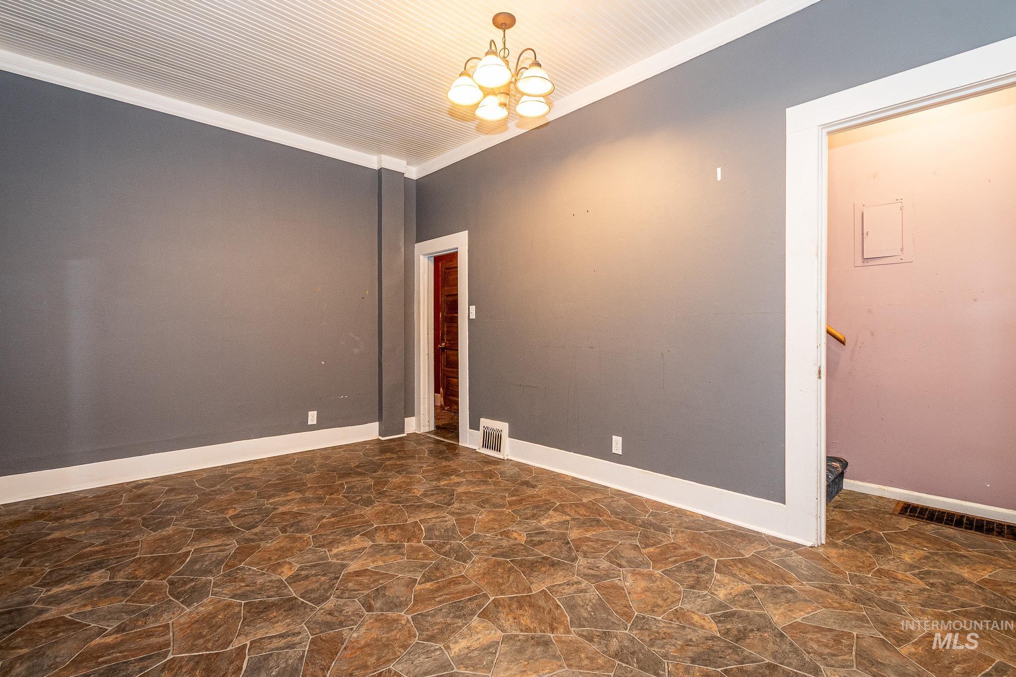 Unfurnished room featuring dark stone finish floors, ornamental molding, and a chandelier