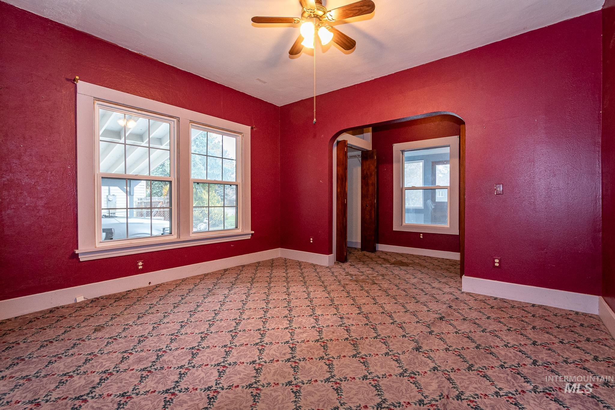 Carpeted empty room with a textured wall, arched walkways, and a ceiling fan