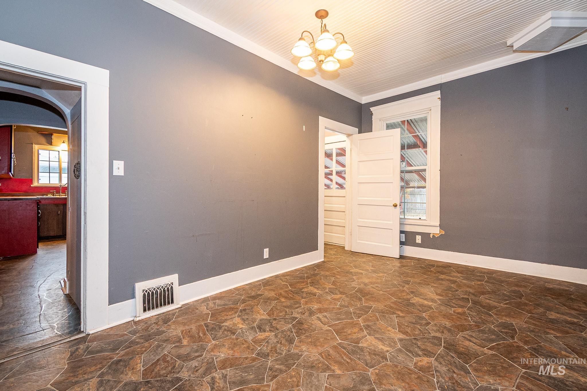 Unfurnished room with stone flooring, healthy amount of natural light, ornamental molding, a chandelier, and arched walkways