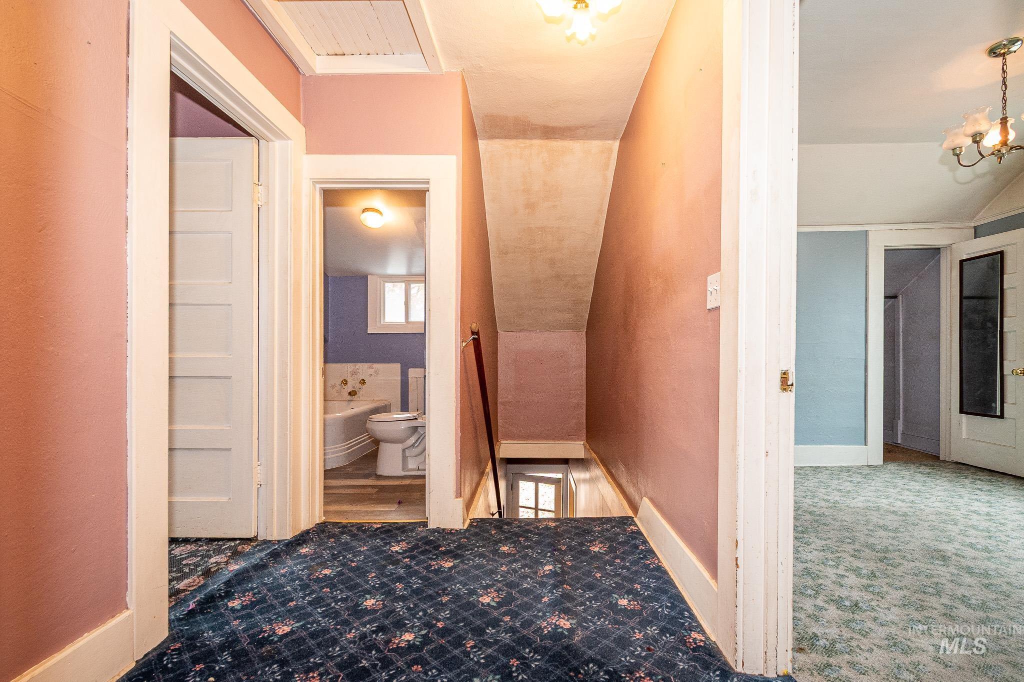 Corridor with vaulted ceiling, an upstairs landing, carpet flooring, and a chandelier