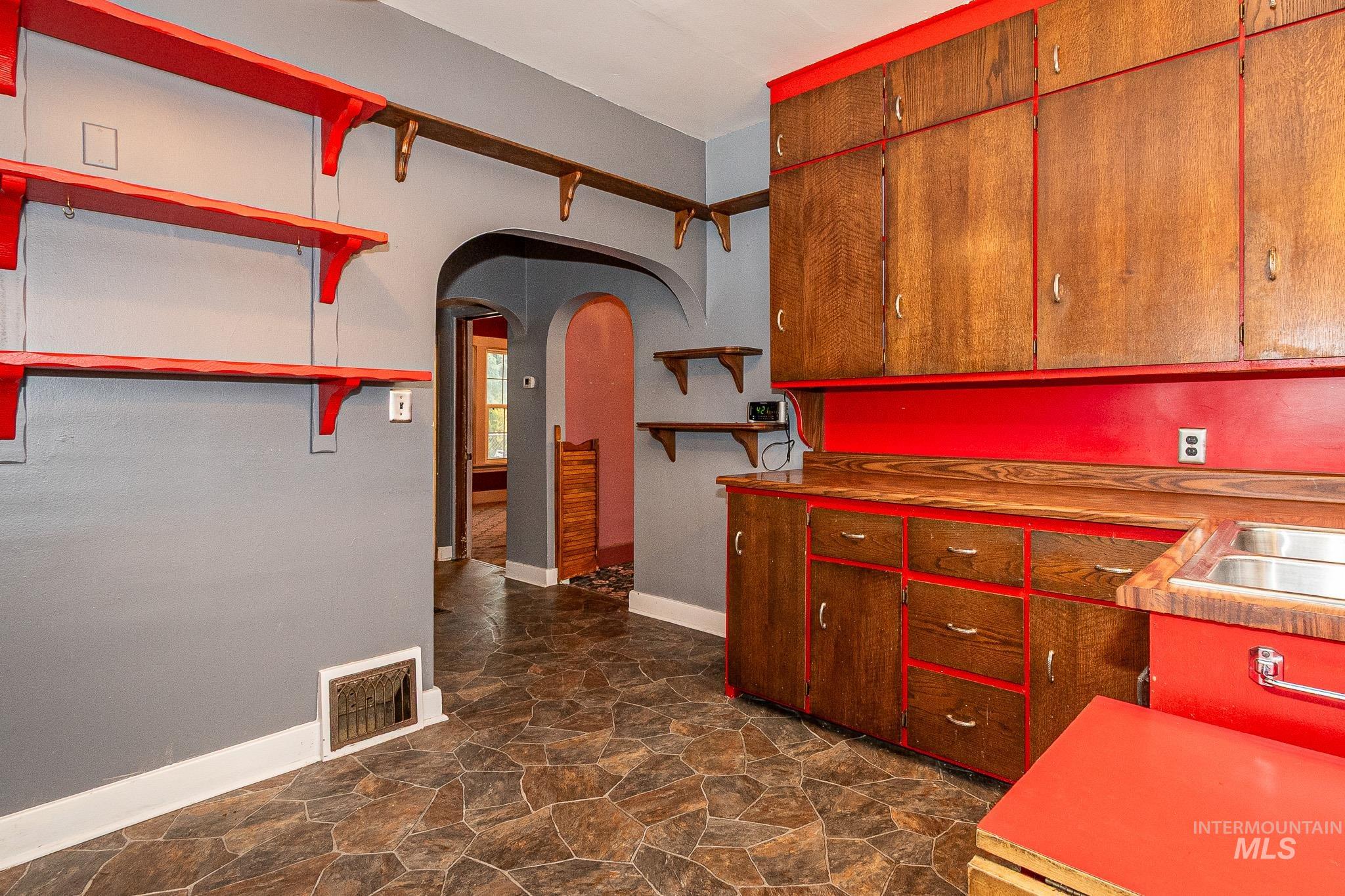Kitchen with arched walkways, dark stone finish flooring, open shelves, and light countertops