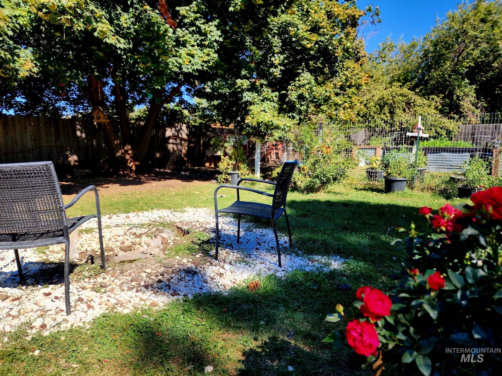 The backyard features a serene seating area framed by roses, trees, and productive garden beds?perfect for entertaining or unwinding.