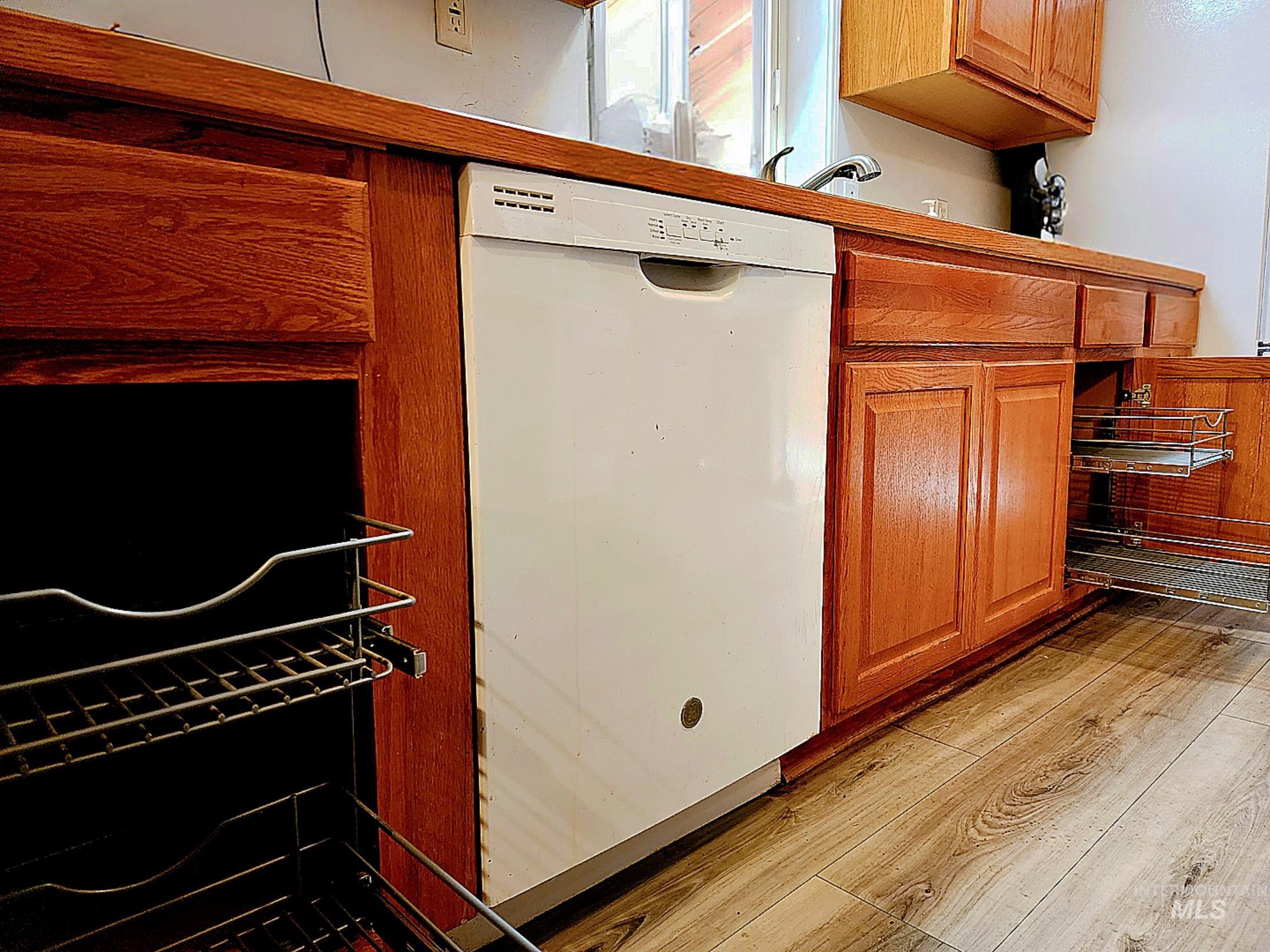 Warm and efficient kitchen featuring rich wood cabinetry, a built-in dishwasher, pull-out storage shelves, and durable plank flooring?perfect for easy everyday living.