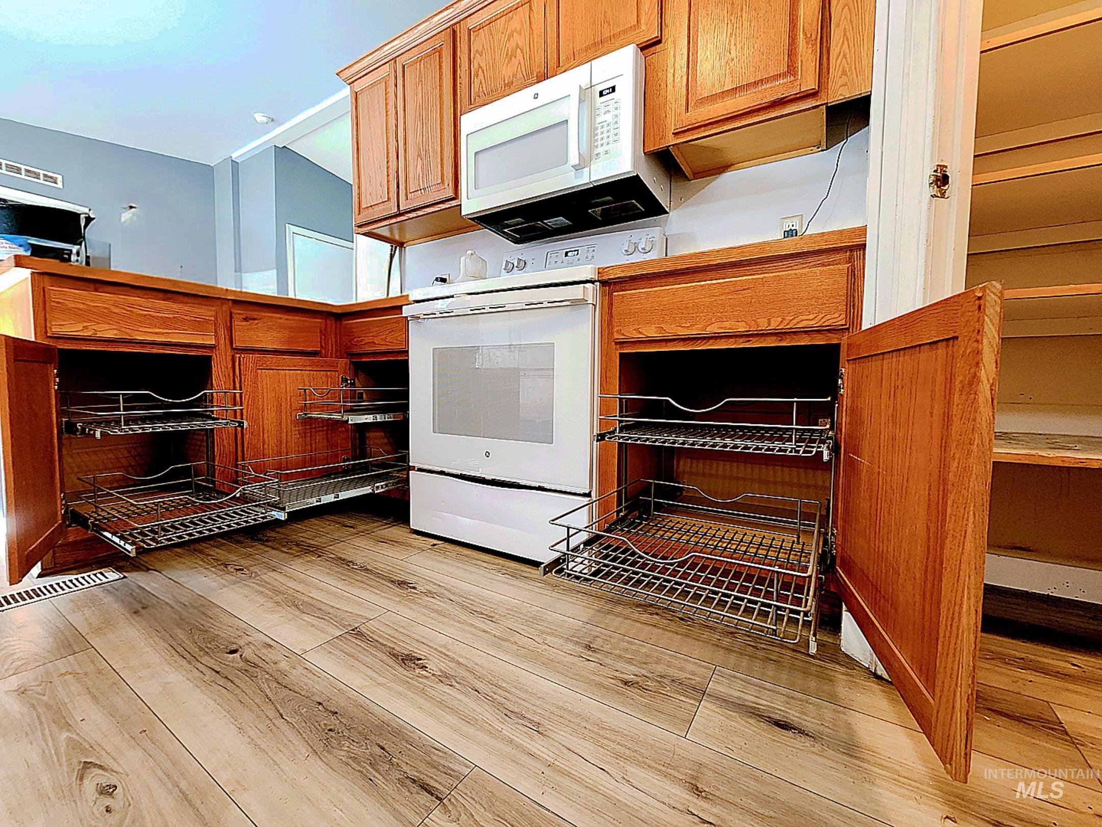 Bright and functional Idaho kitchen featuring pull-out cabinet shelves, warm wood cabinetry, modern appliances, and durable plank flooring designed for easy living.