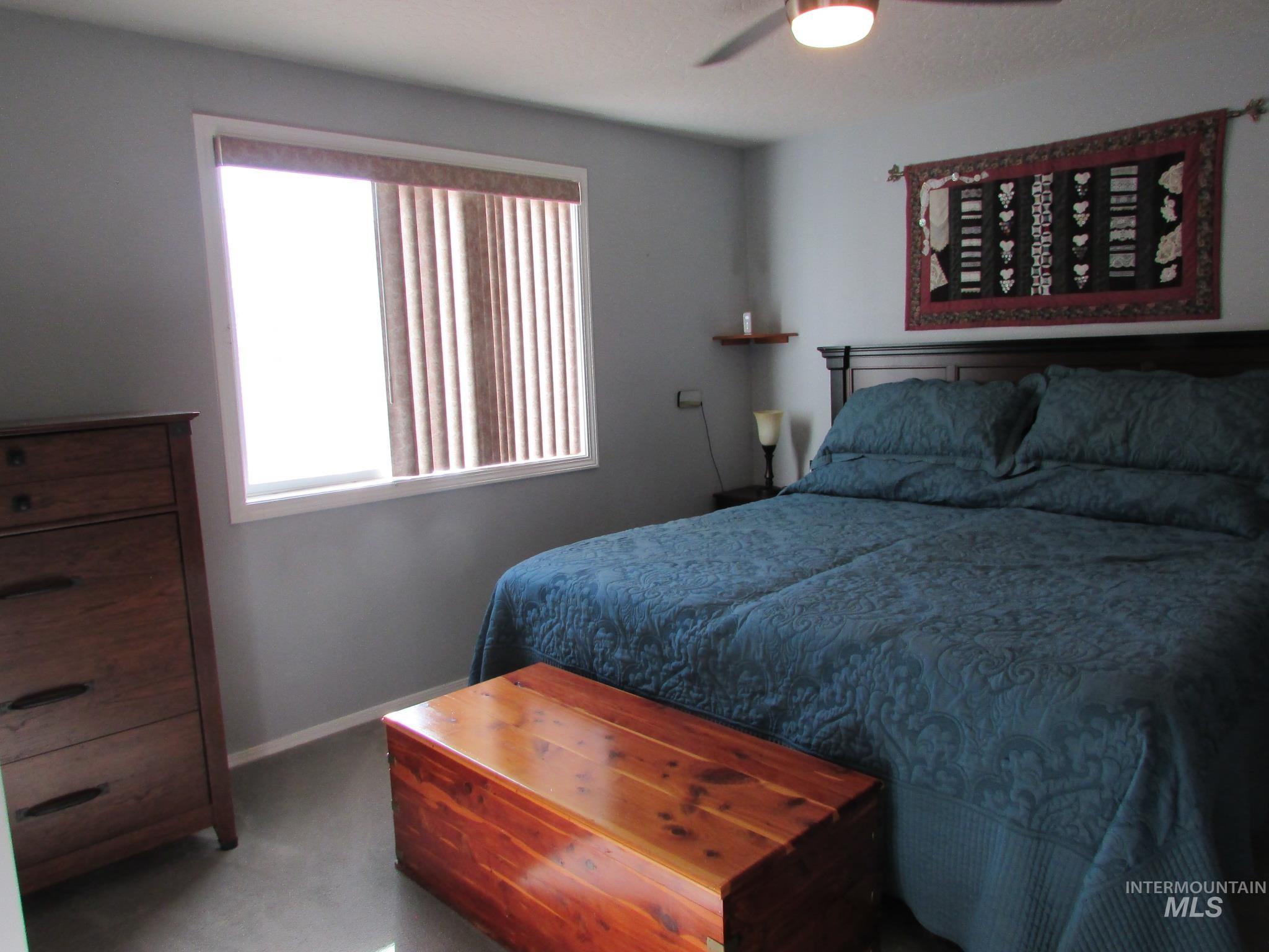 Bedroom featuring a window with vertical blinds, a ceiling fan with integrated lighting, a dark wood-finish headboard, and light gray wall paint