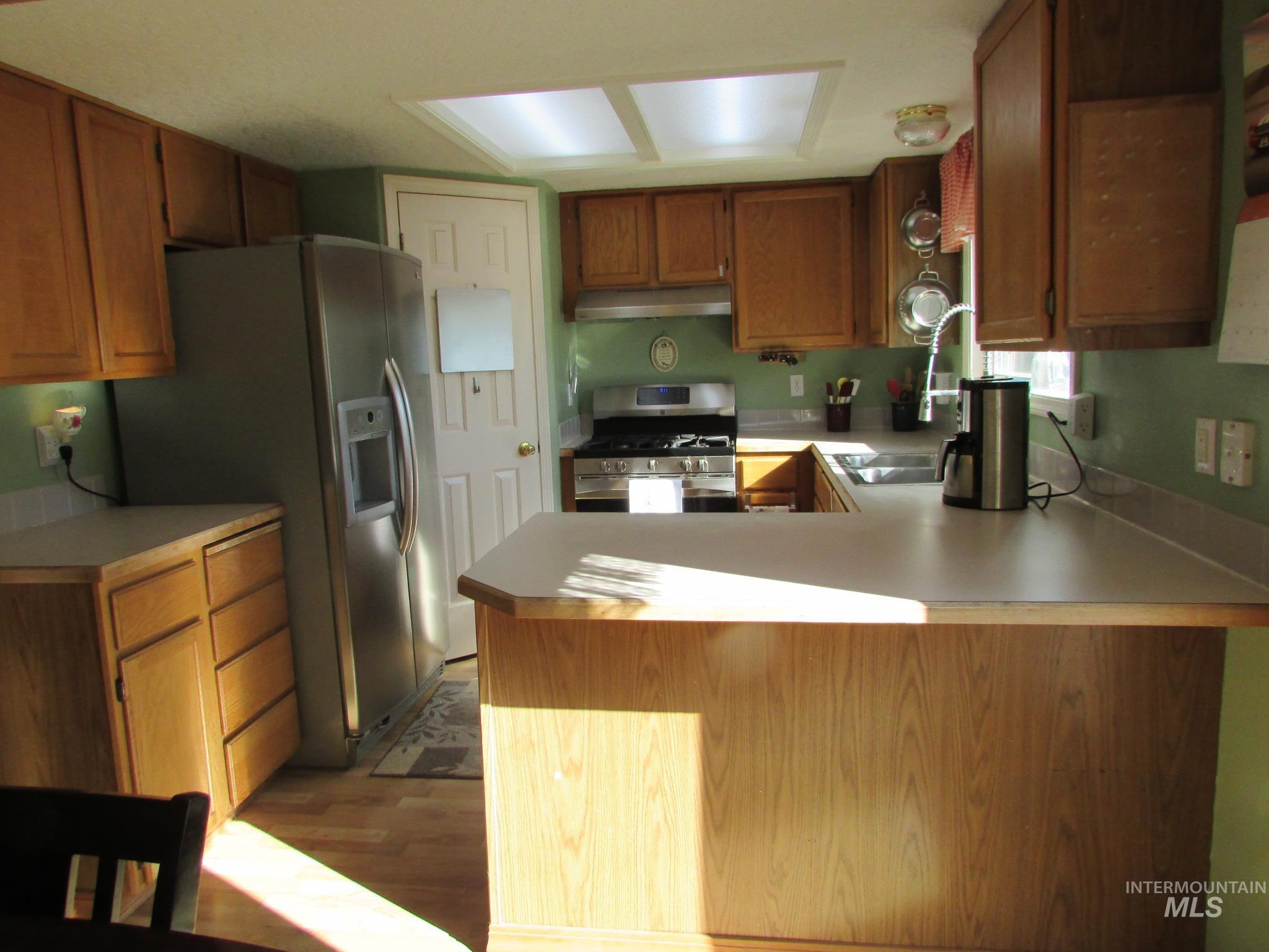 Kitchen featuring wood-finish cabinetry, light-toned countertops, and a stainless steel refrigerator