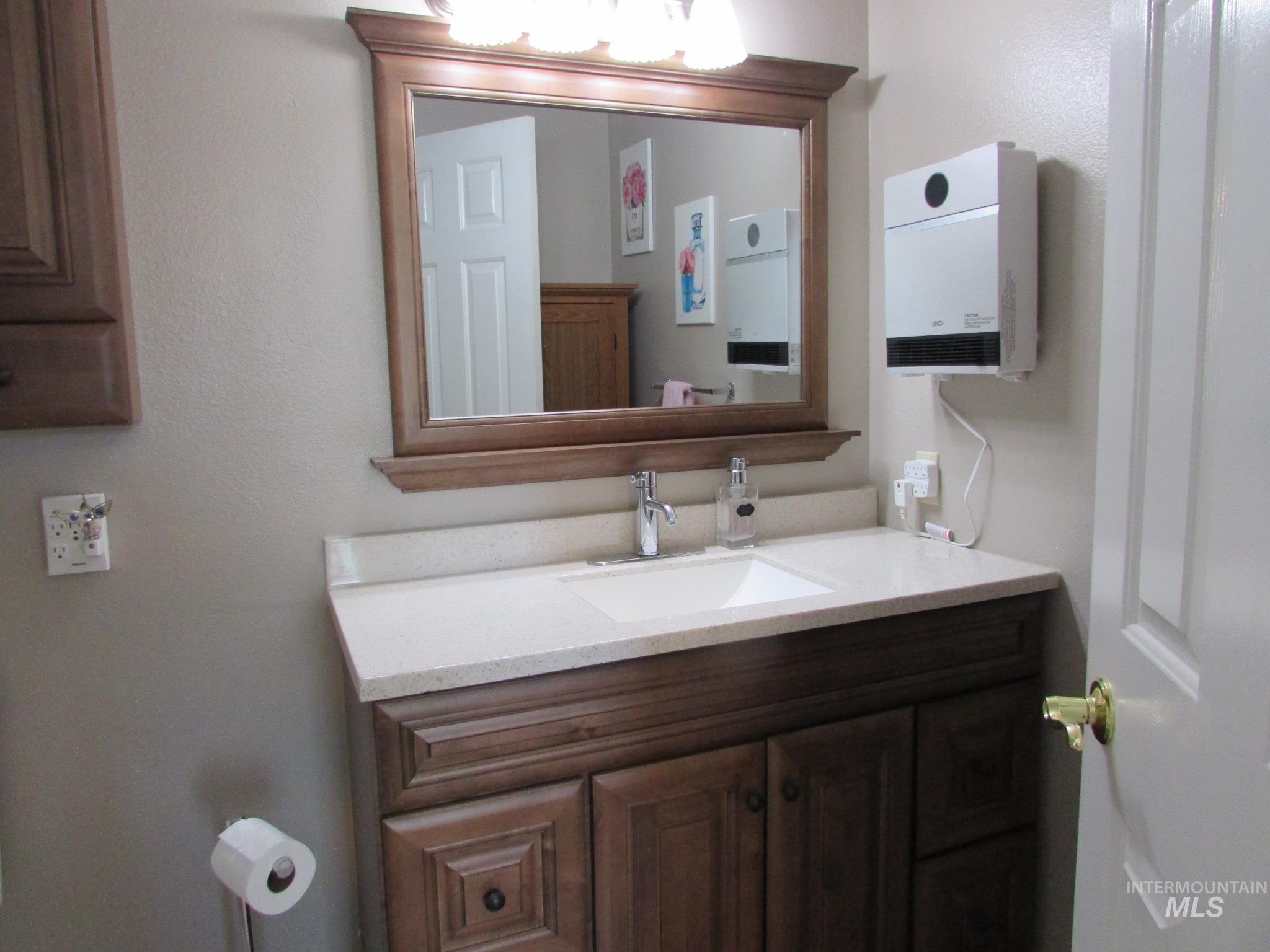 Bathroom vanity featuring a wood-finish cabinet, integrated sink, and light-toned countertop with a matching backsplash
