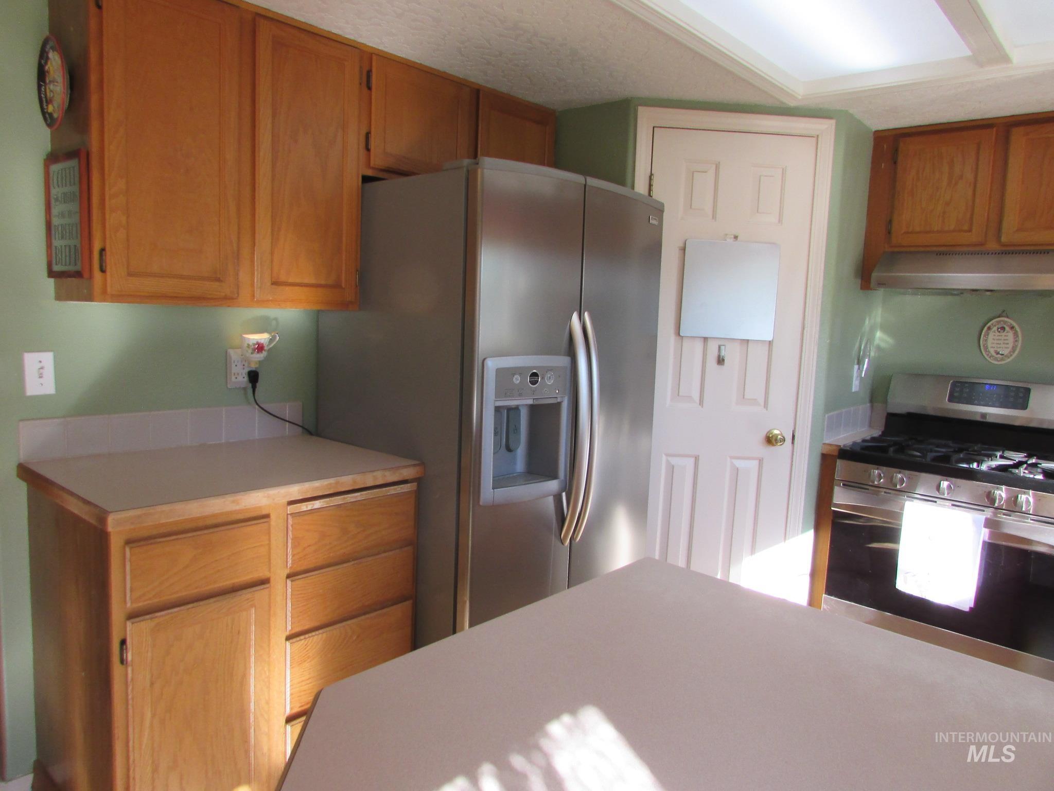 Kitchen featuring wood cabinetry, stainless steel refrigerator with water and ice dispenser, stainless steel gas range, and a neutral countertop