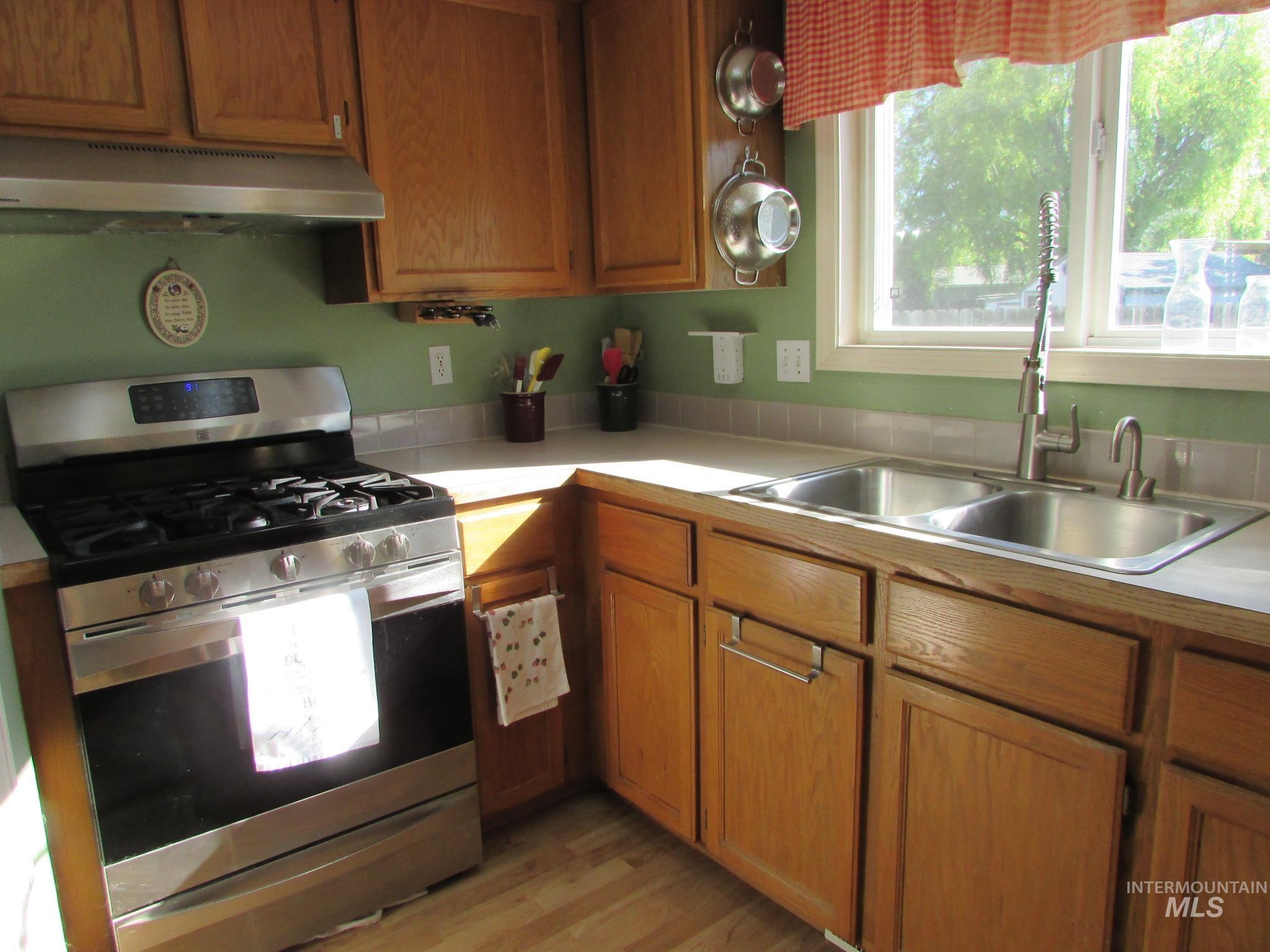 Kitchen featuring wood cabinetry, stainless steel appliances, a double basin sink with a pull-down faucet, a light-toned countertop, and a tiled backsplash