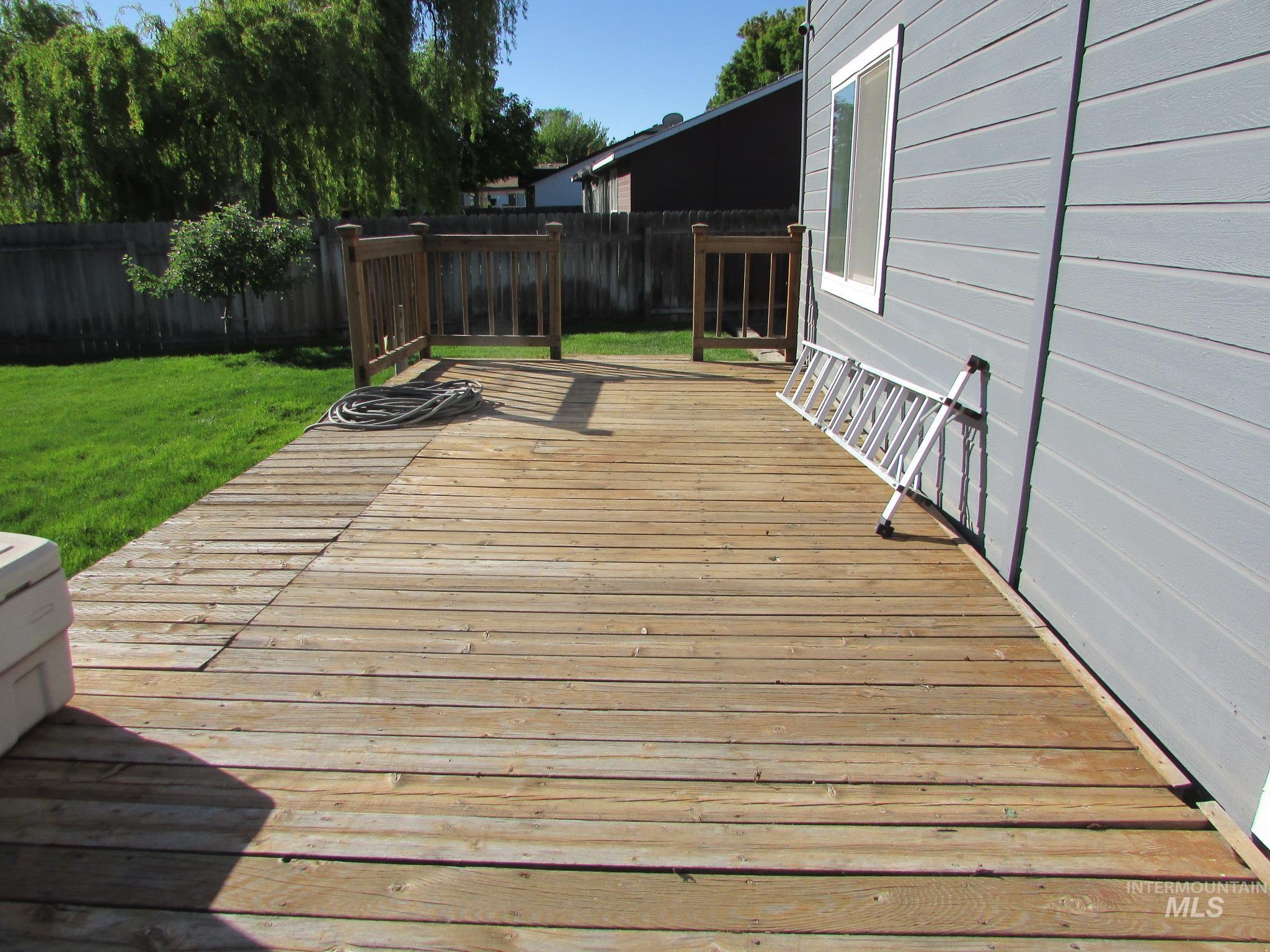 Spacious outdoor deck with natural wood planks, a partial wooden railing, and a gray horizontal siding exterior