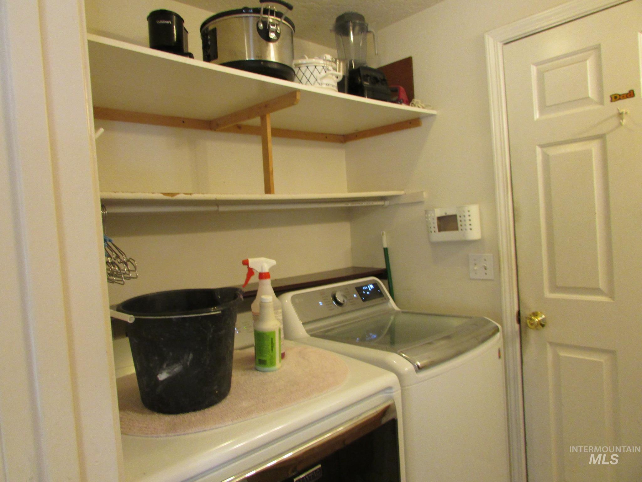 Laundry area featuring multiple wall-mounted shelves, a built-in countertop, and a paneled white door with a brass-finish doorknob