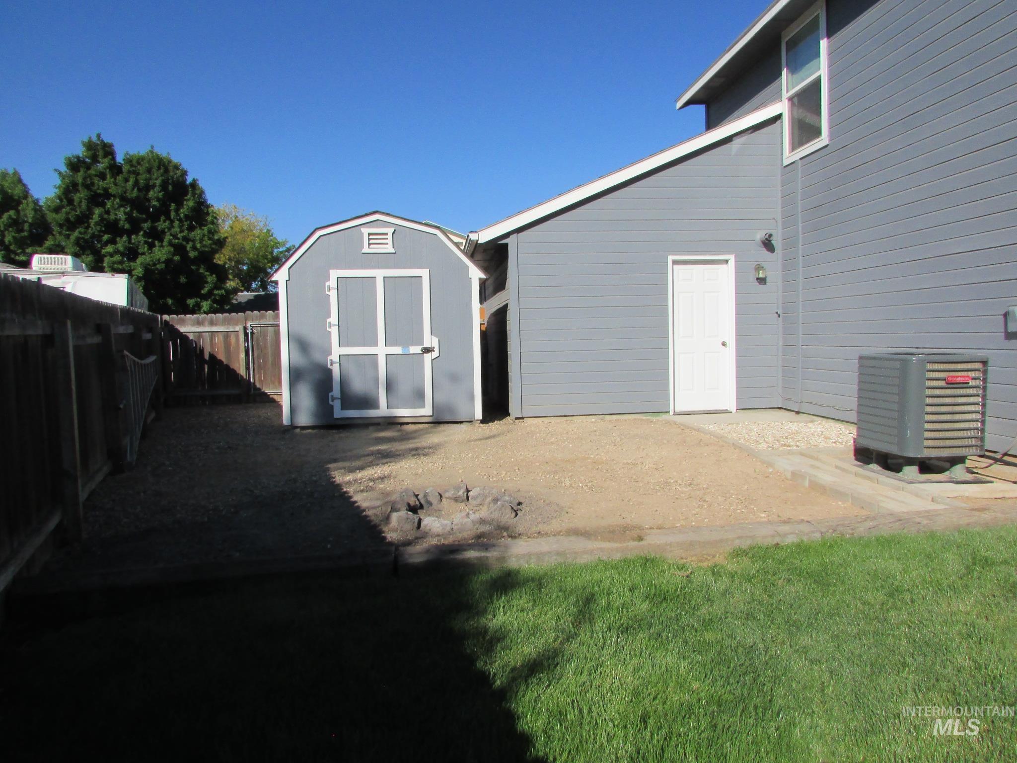 Backyard featuring a gray storage shed with white trim, a privacy fence, and a gravel area with partial lawn