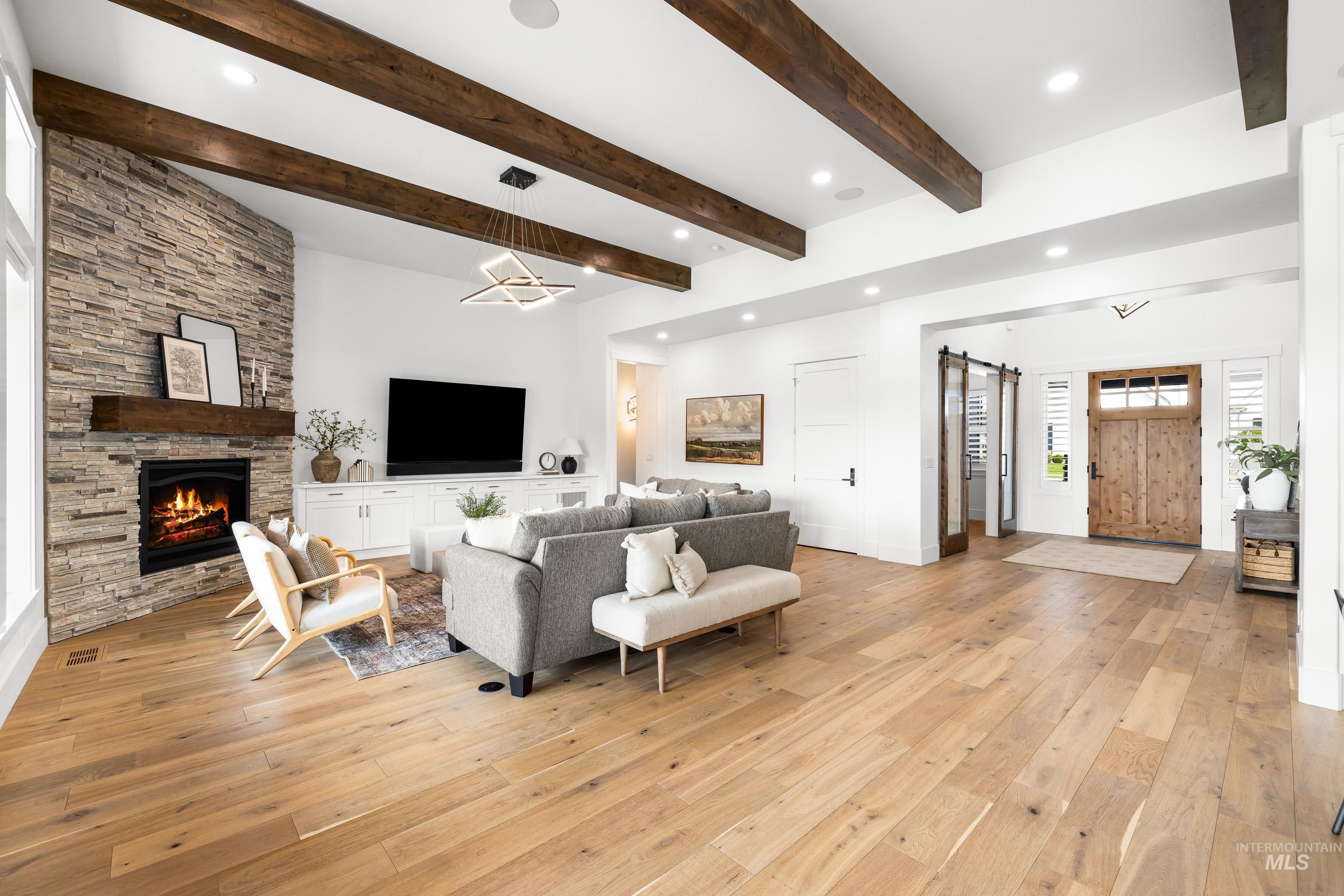 Living area with a barn door, light wood-type flooring, a fireplace, beamed ceiling, and recessed lighting