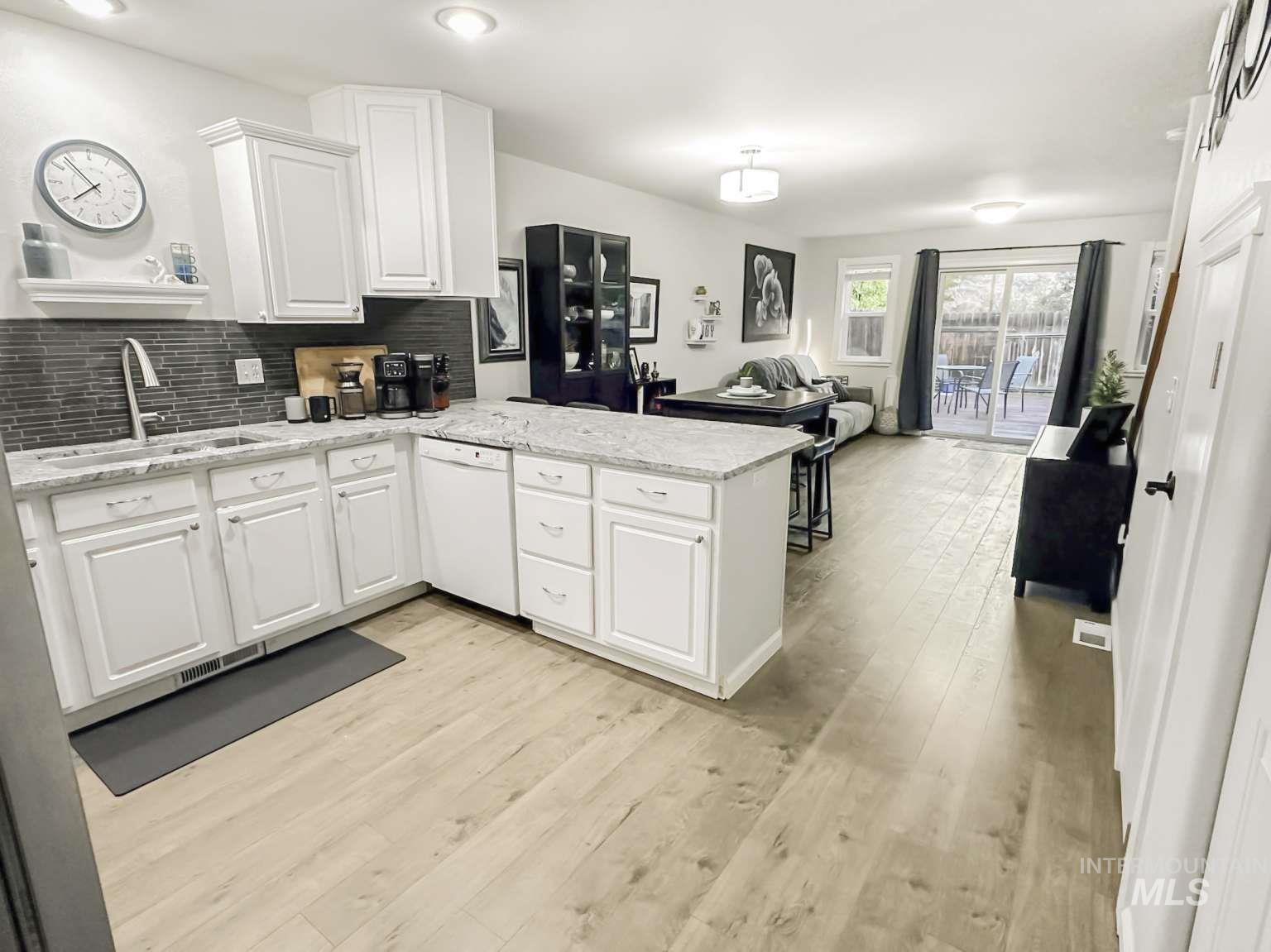 Kitchen with tasteful backsplash, a peninsula, open floor plan, white cabinets, and light wood-type flooring