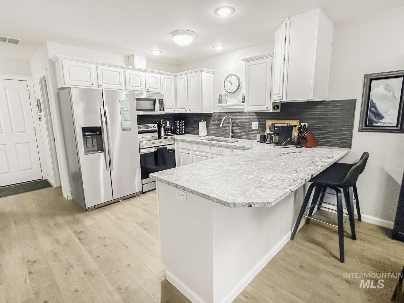 Kitchen with stainless steel appliances, a peninsula, white cabinetry, a kitchen breakfast bar, and light wood finished floors